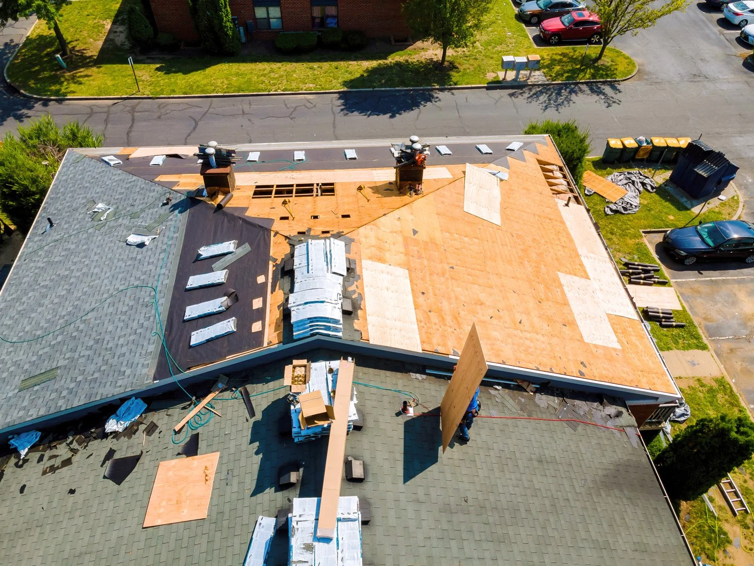 Aerial view of a building roof under construction, with some sections partially stripped and new roofing materials being installed.