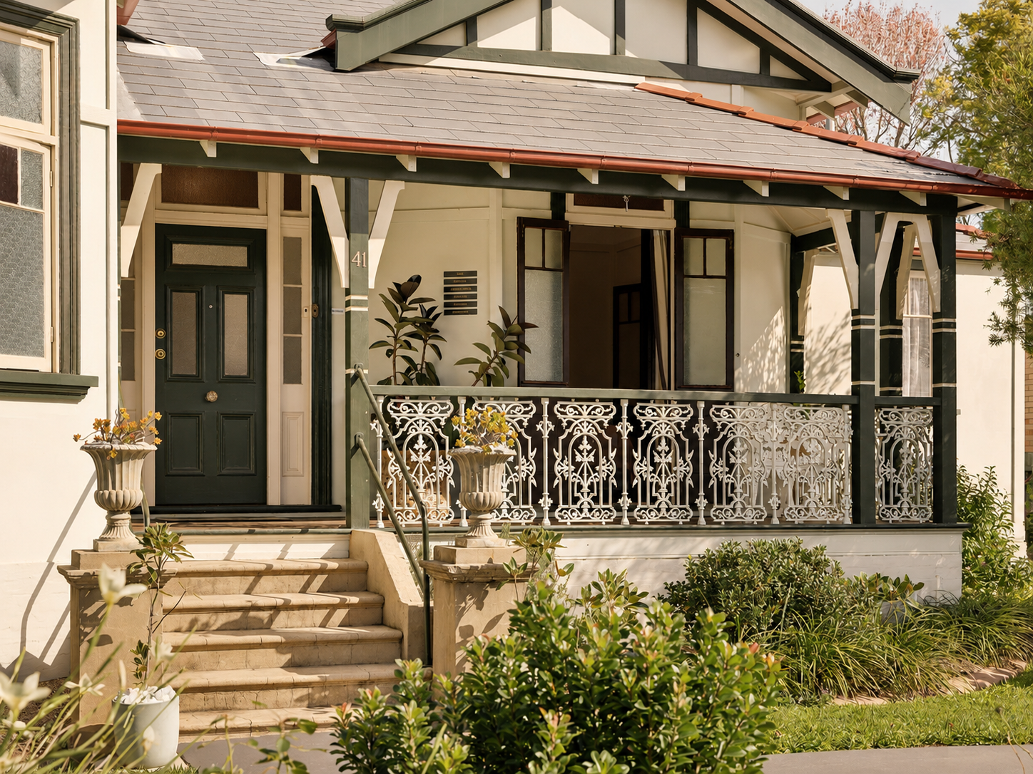 Front porch of a house with decorative white metal railing, black door, and potted plants.