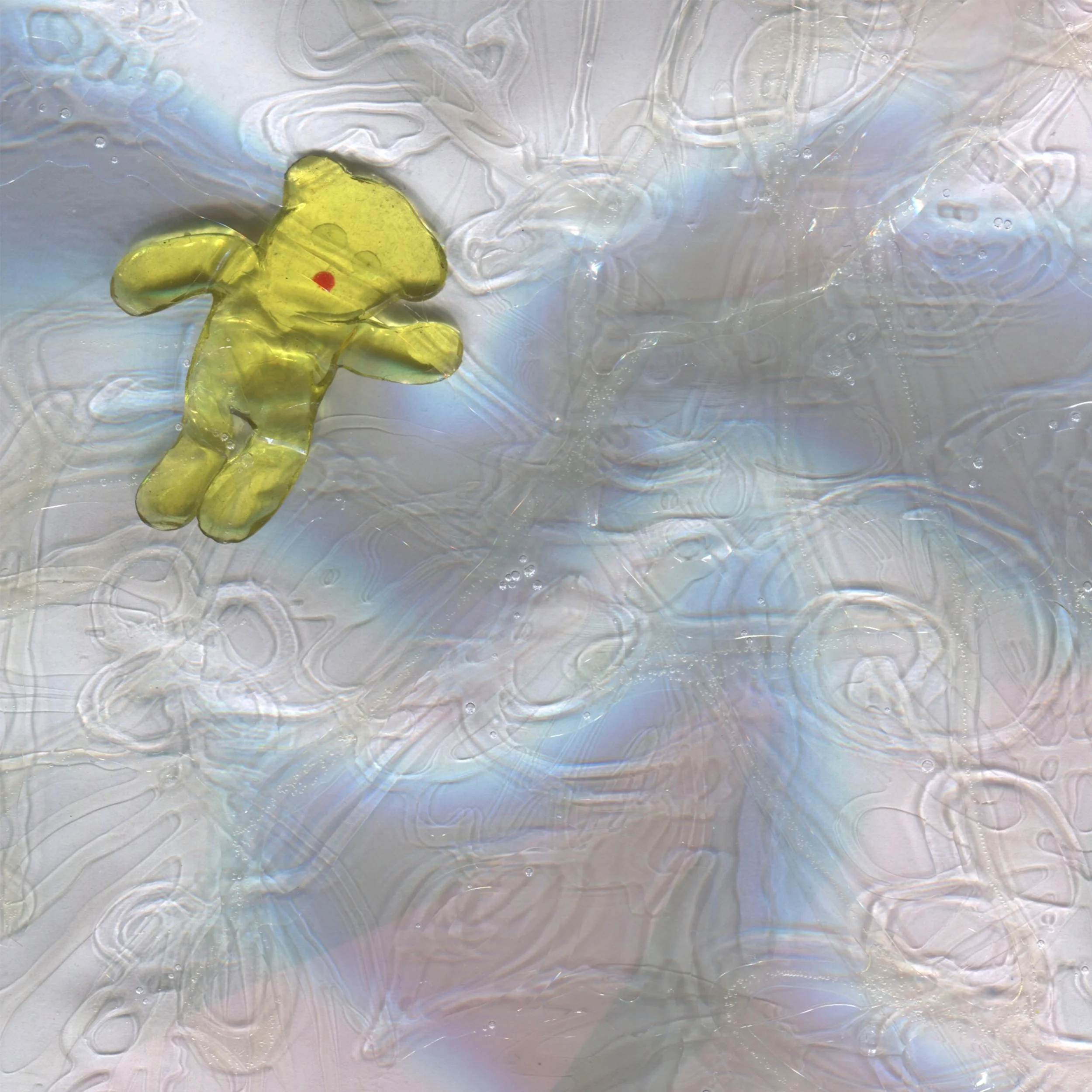 Close-up of a yellow bear laying on a glass surface with iridescent refractions.
