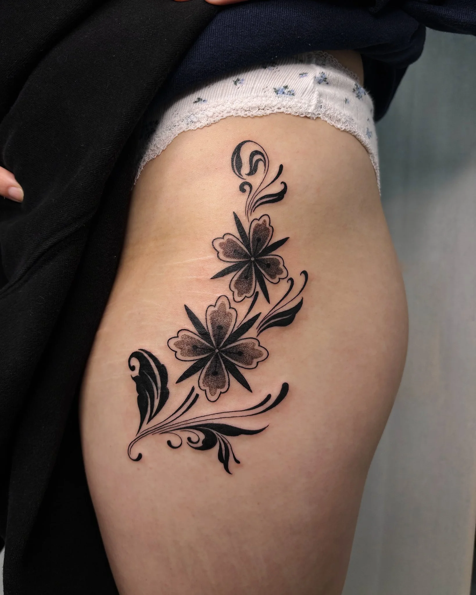 Tattoo of a butterfly with swirling floral and abstract decorative elements on a person's thigh.