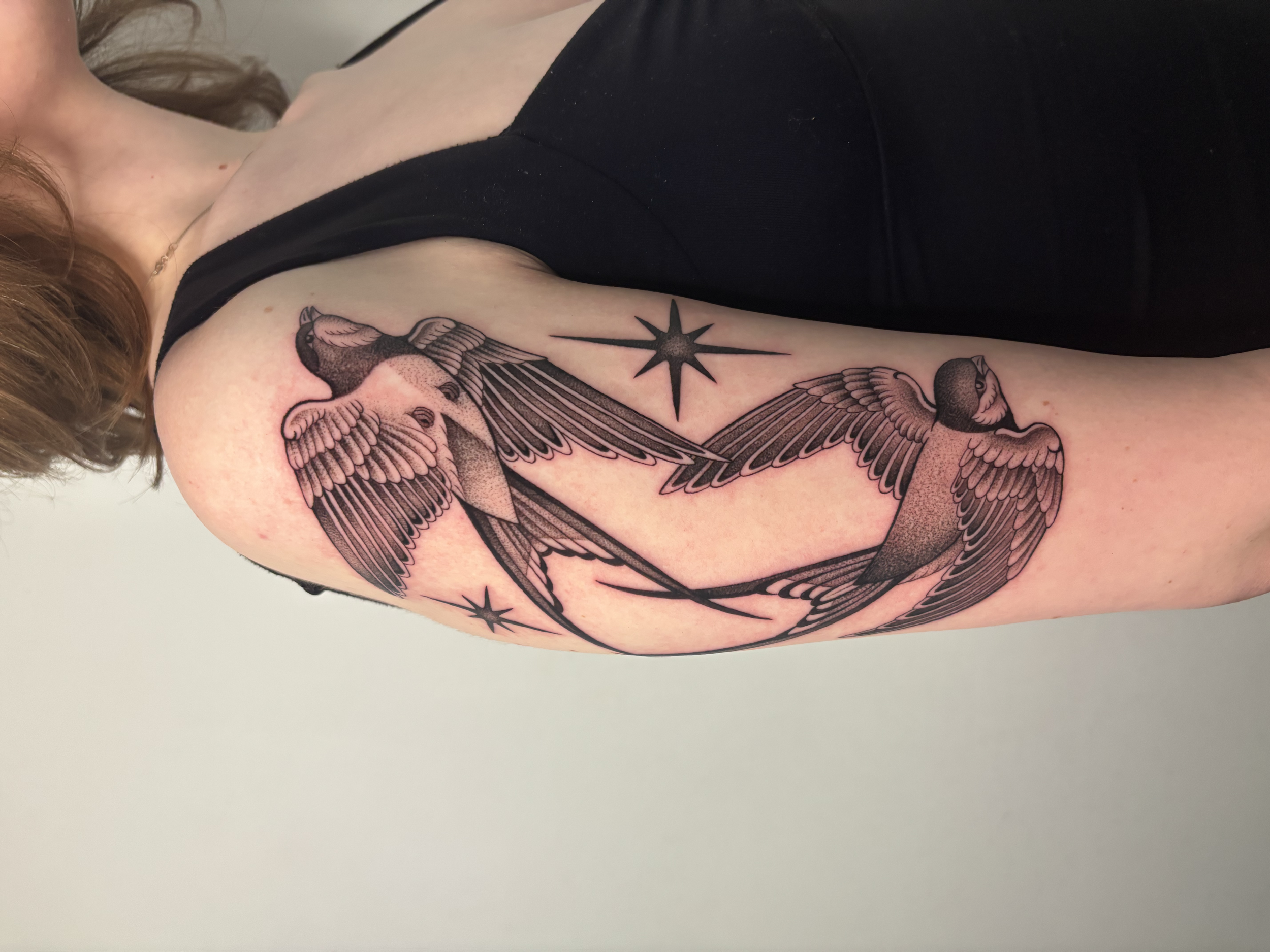 A tattoo of three birds with spread wings flying across a person's upper arm and shoulder, with a starburst symbol next to them.