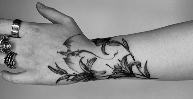 Close-up of a hand with multiple rings, featuring a floral tattoo on the forearm.