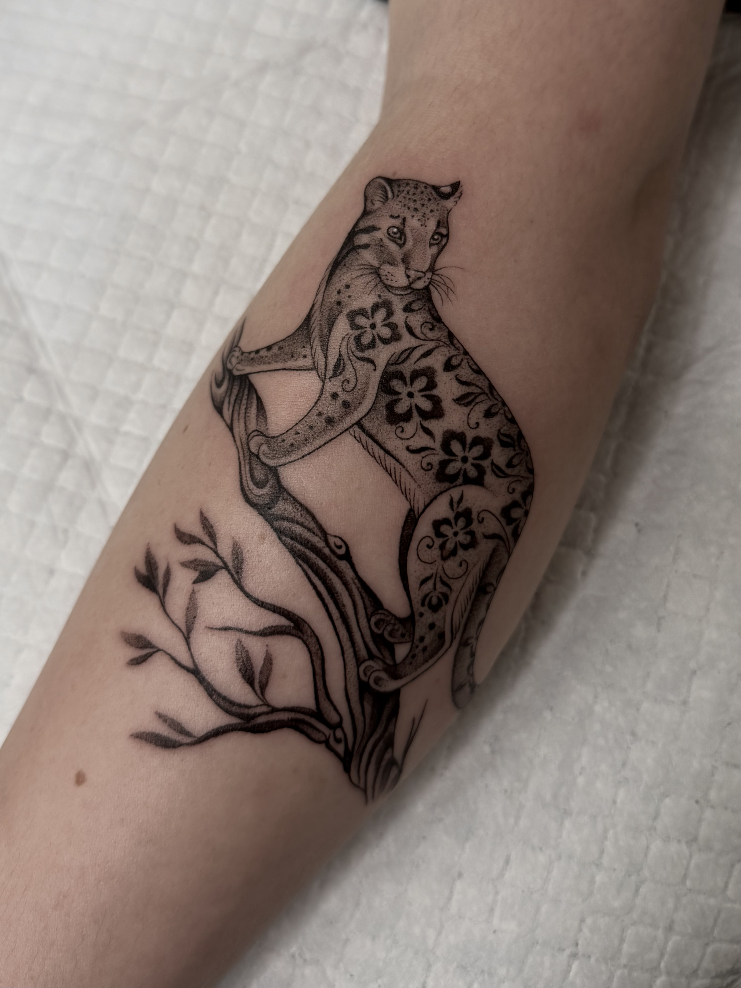 A tattoo of a leopard with floral and vine details on a person's forearm.
