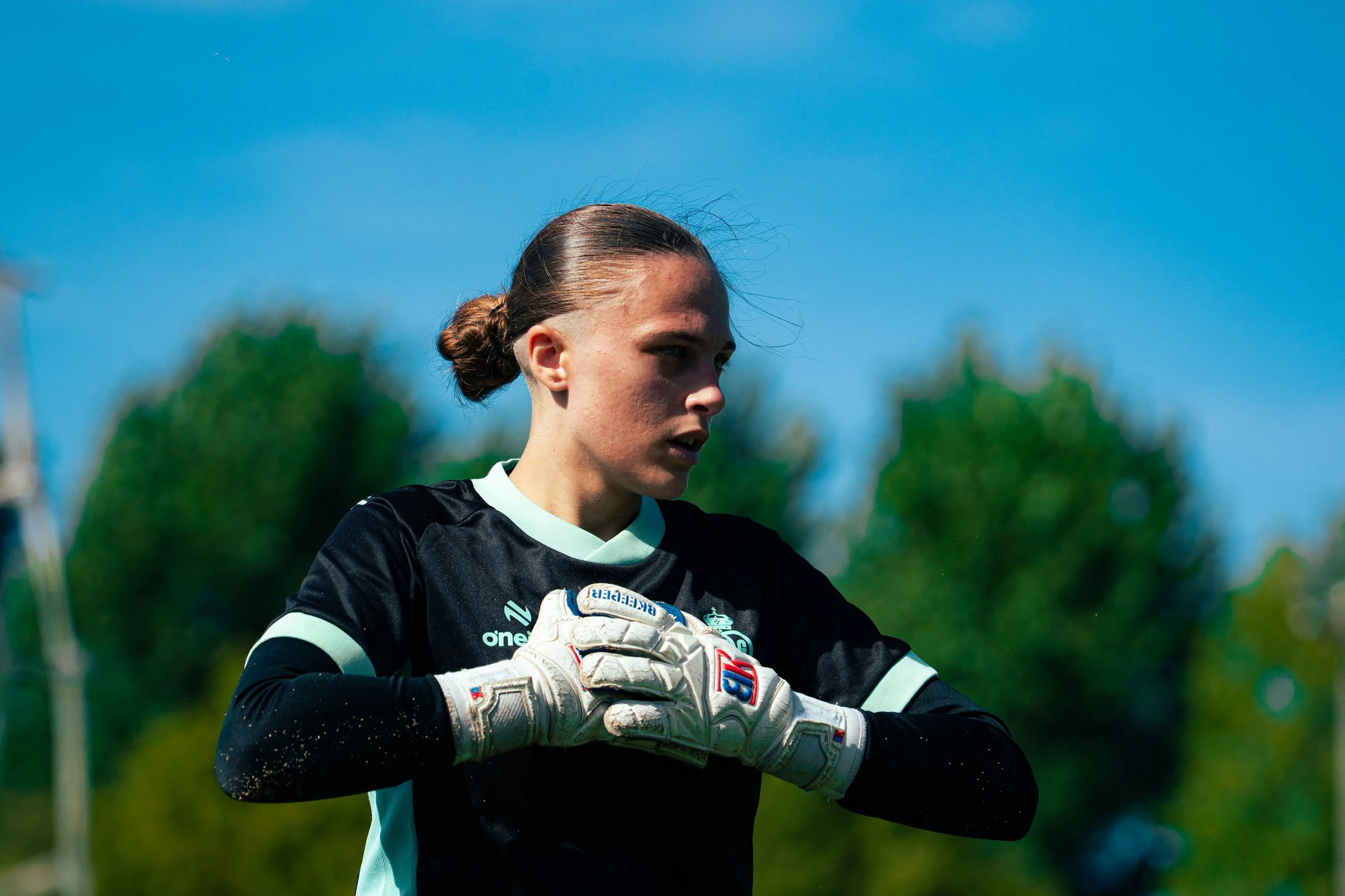 Female soccer goalkeeper adjusting gloves outdoors on a sunny day.