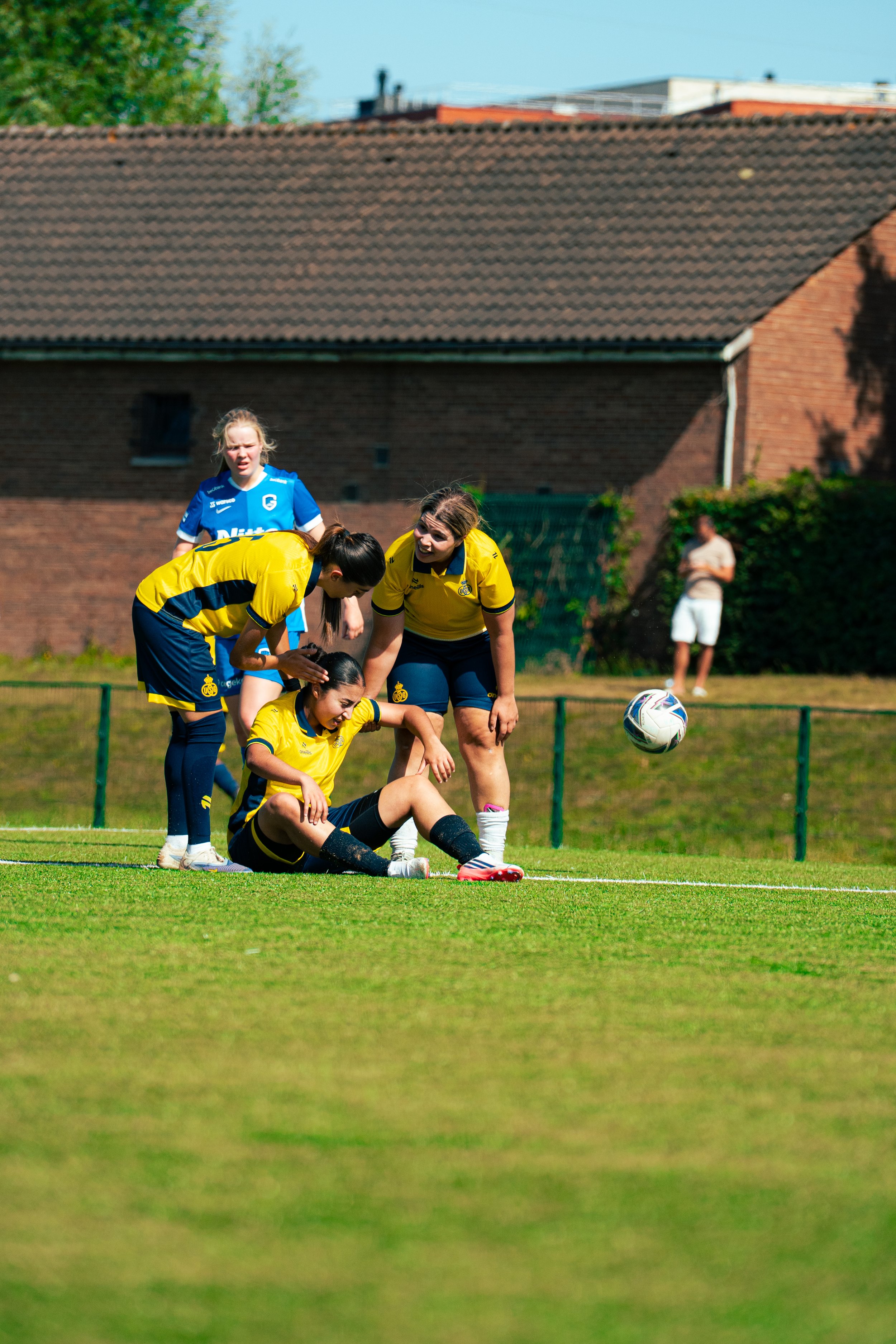 Female soccer players assisting an injured teammate on the field during a match.