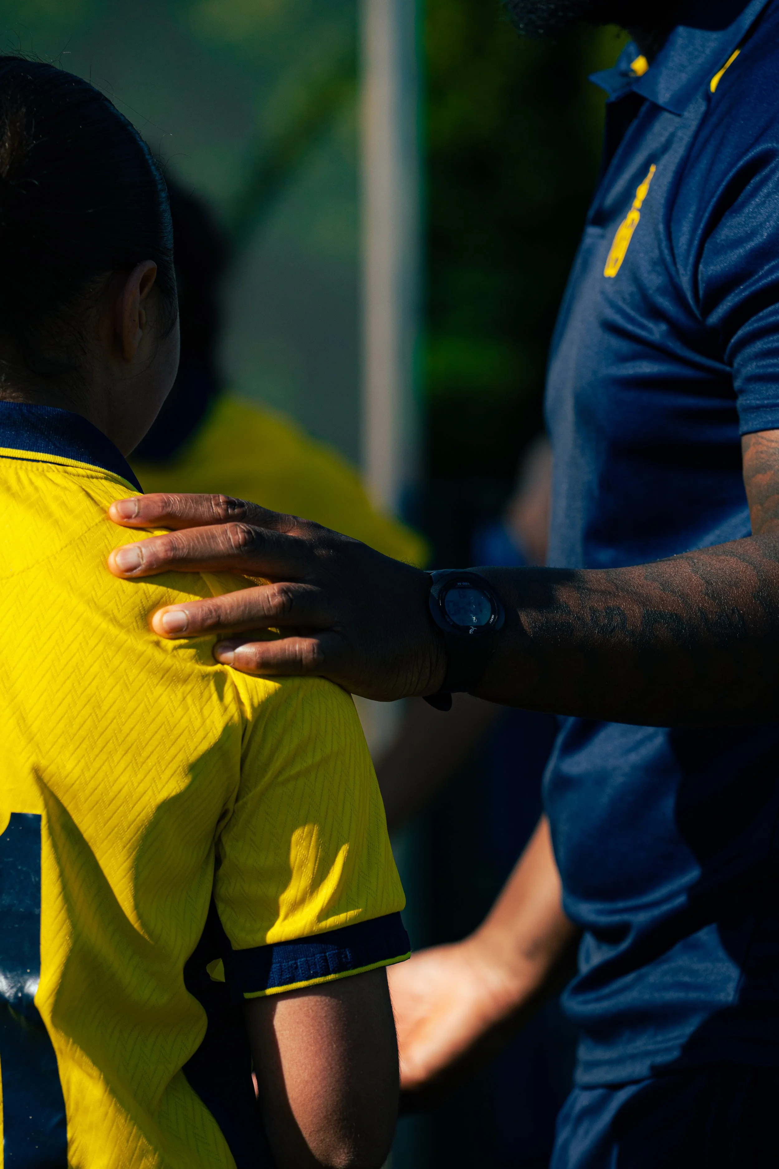 A person in a yellow sports jersey being comforted or consoled by another person in a blue shirt, with the other's hand on their shoulder.