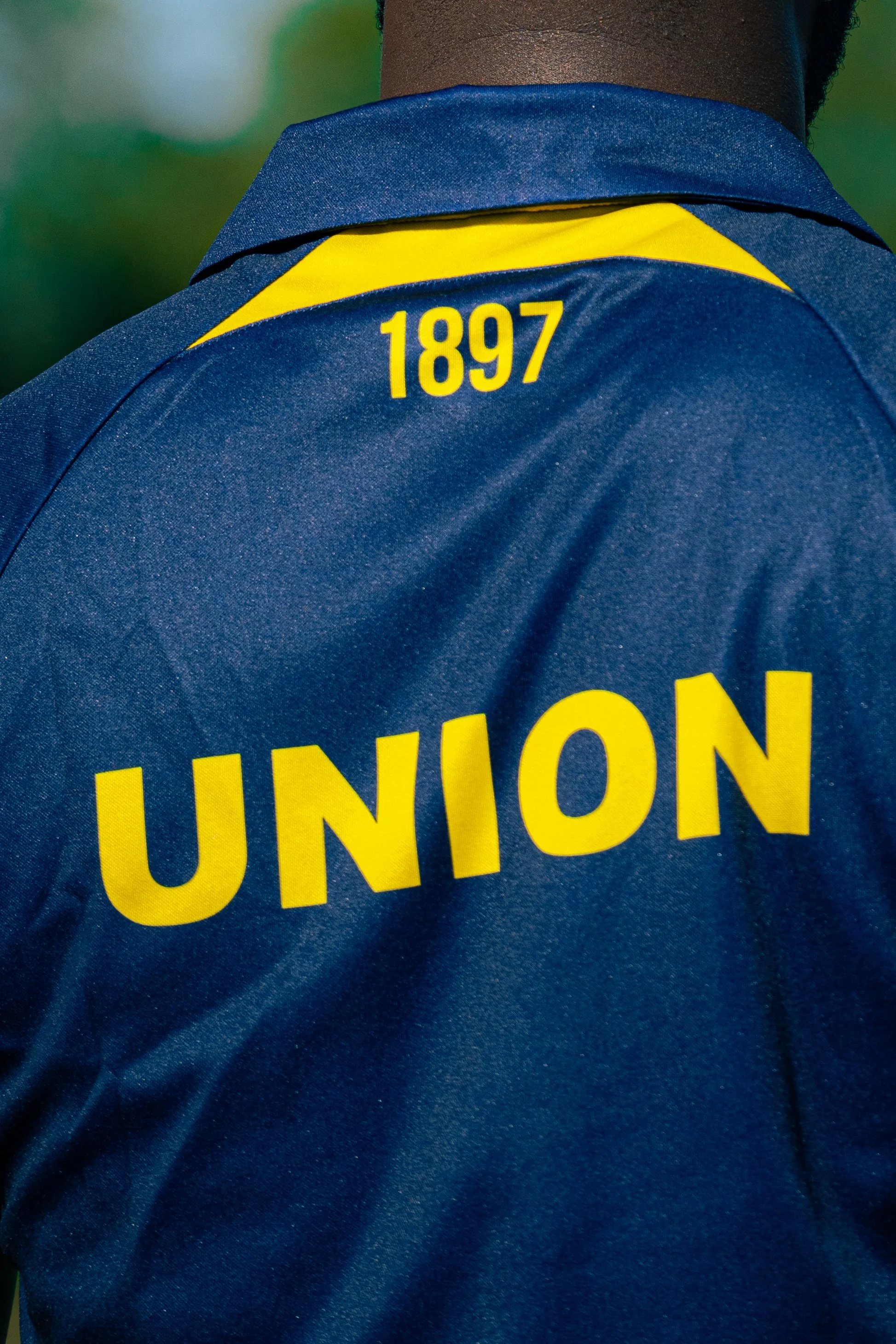 Close-up of a person's back wearing a blue jacket with yellow text and numbers, including the words 'UNION' and the numbers '1897' on the back.