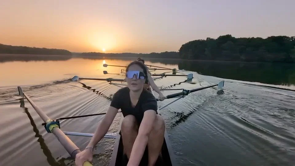 A group of women in a rowing boat practicing on a calm river at sunset.