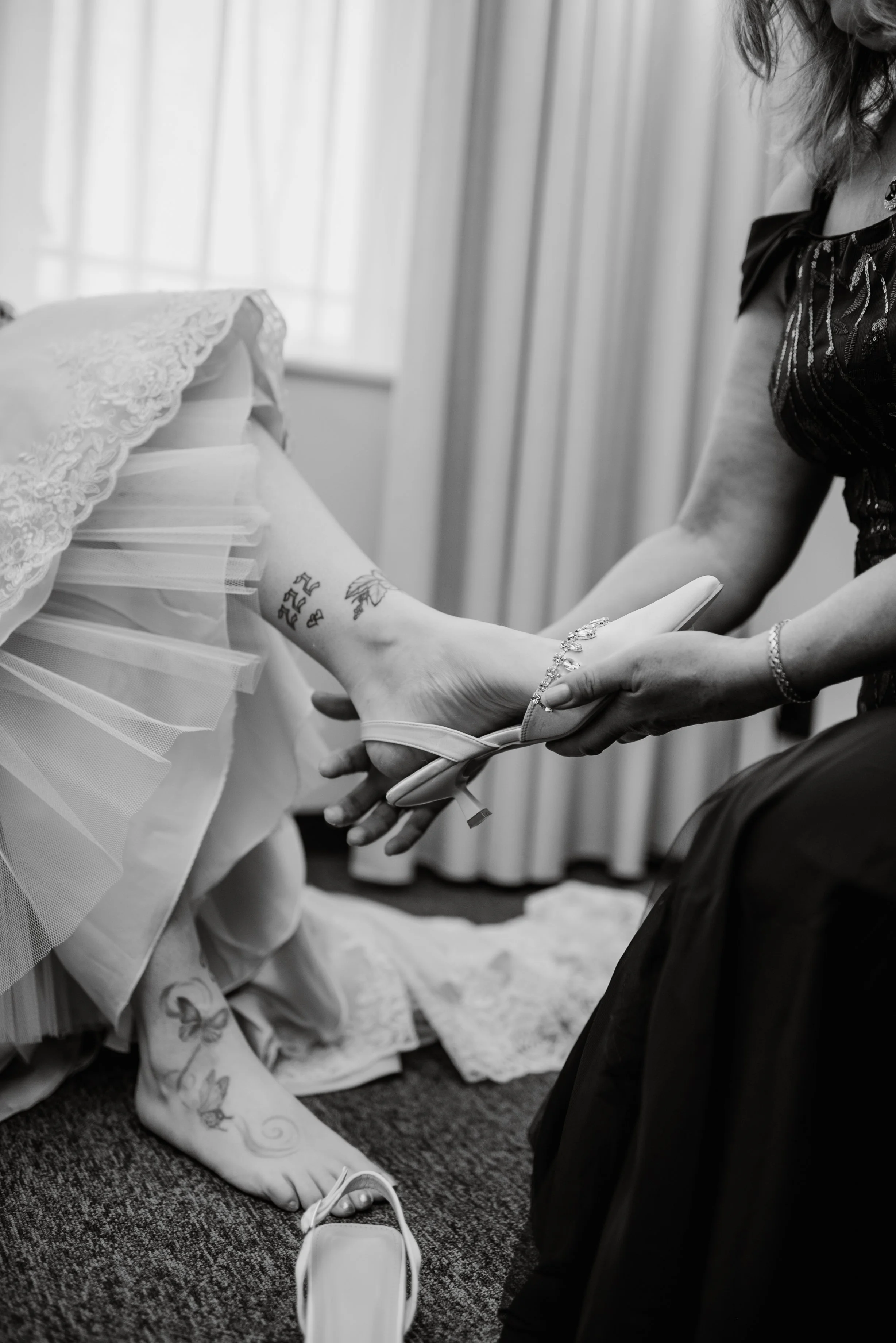 A person is helping another person with a wedding dress or formal gown, tying or adjusting their shoe.