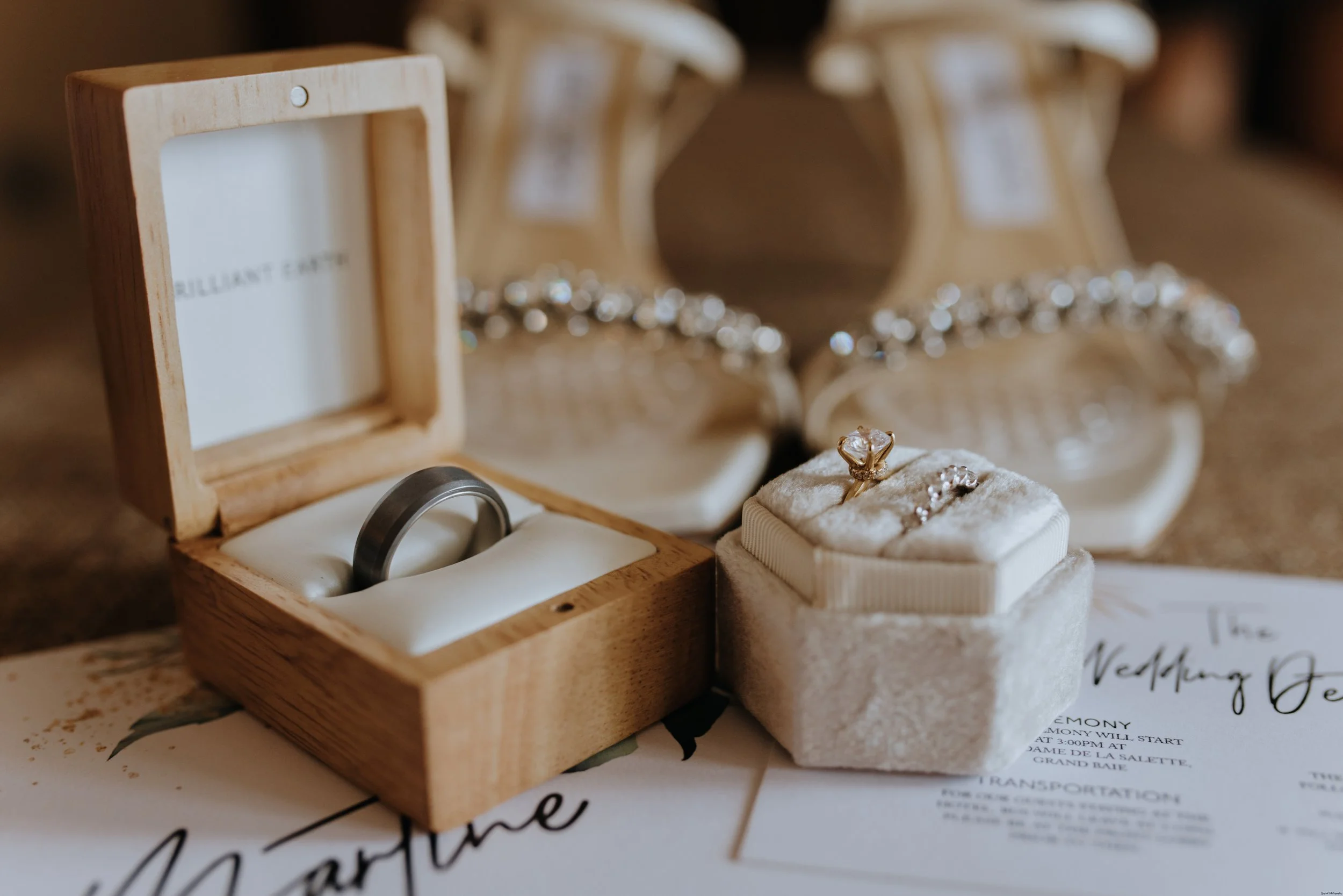 A wedding ring and a diamond ring inside a small wooden box, placed on a table with wedding details.
