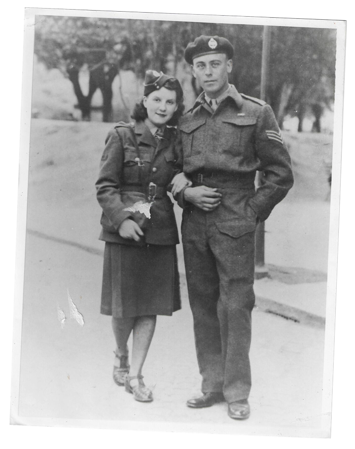 Black and white photo of a young woman in military uniform and a man in military uniform standing together outdoors, smiling, with trees in the background.