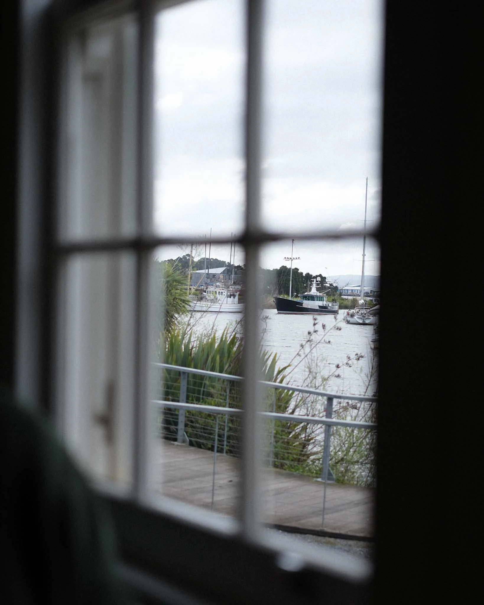 View of a marina with boats docked by water, seen through a window or grille with bars, during an overcast day.
