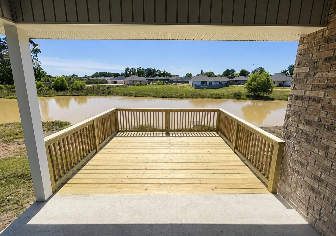 View of a freshly built wooden deck overlooking a pond with houses in the background under a clear blue sky.