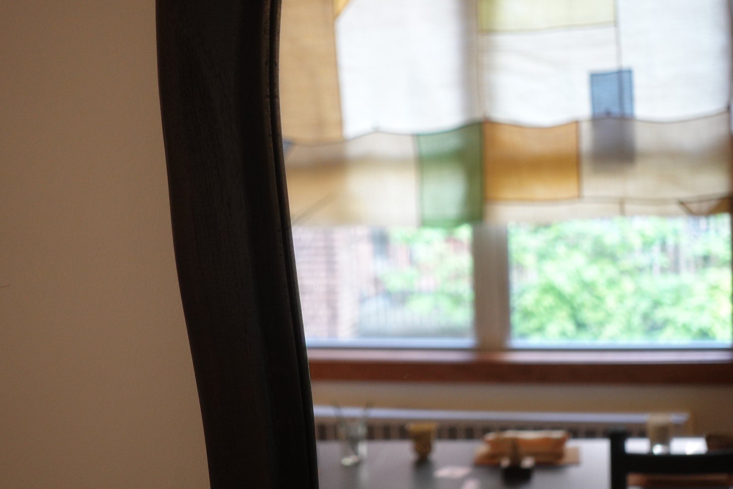 Close-up of a black horizontal surface with a background view of a window with patterned curtains and an interior room with furniture.