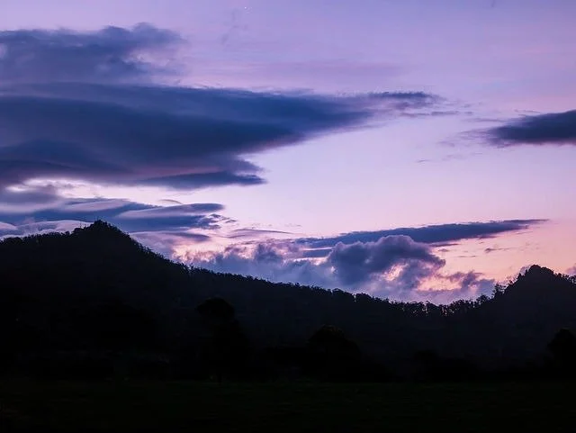 Sunset or sunrise over a mountainous landscape with purple and pink clouds in the sky.