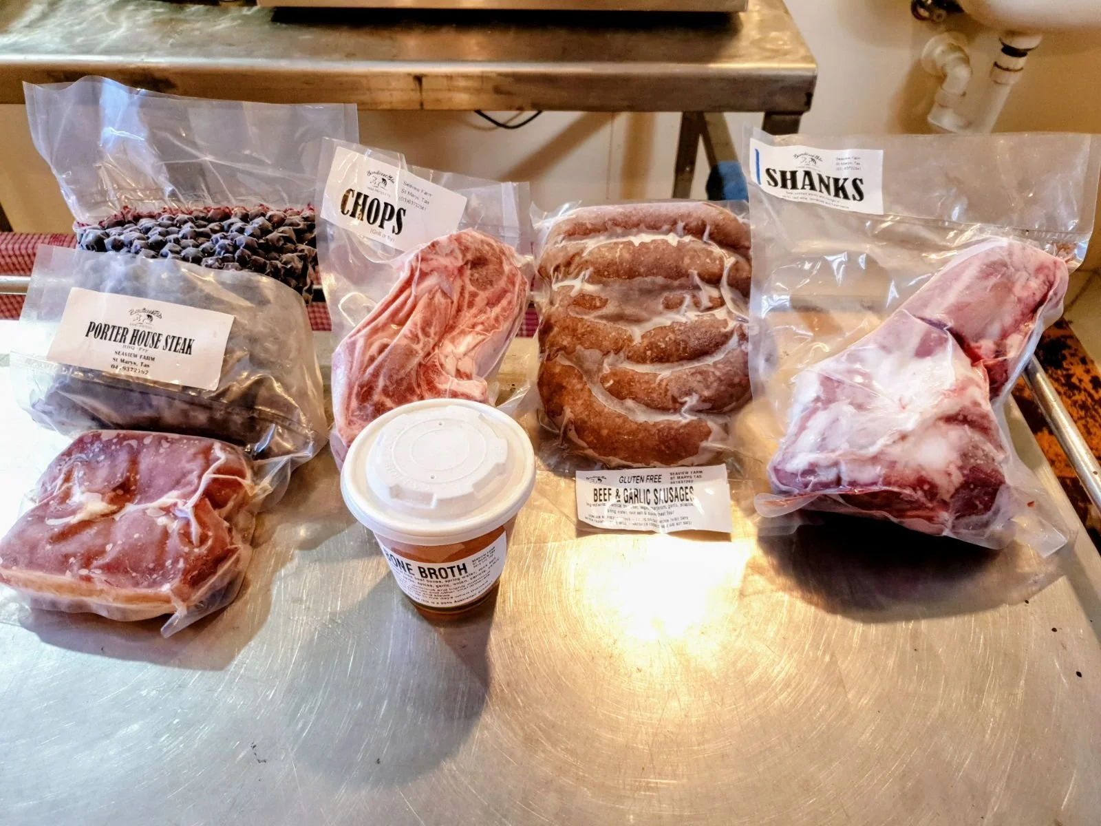 Various cuts of raw meat, including pork, sausage, shank, beef broth, and black beans, on a stainless steel table.