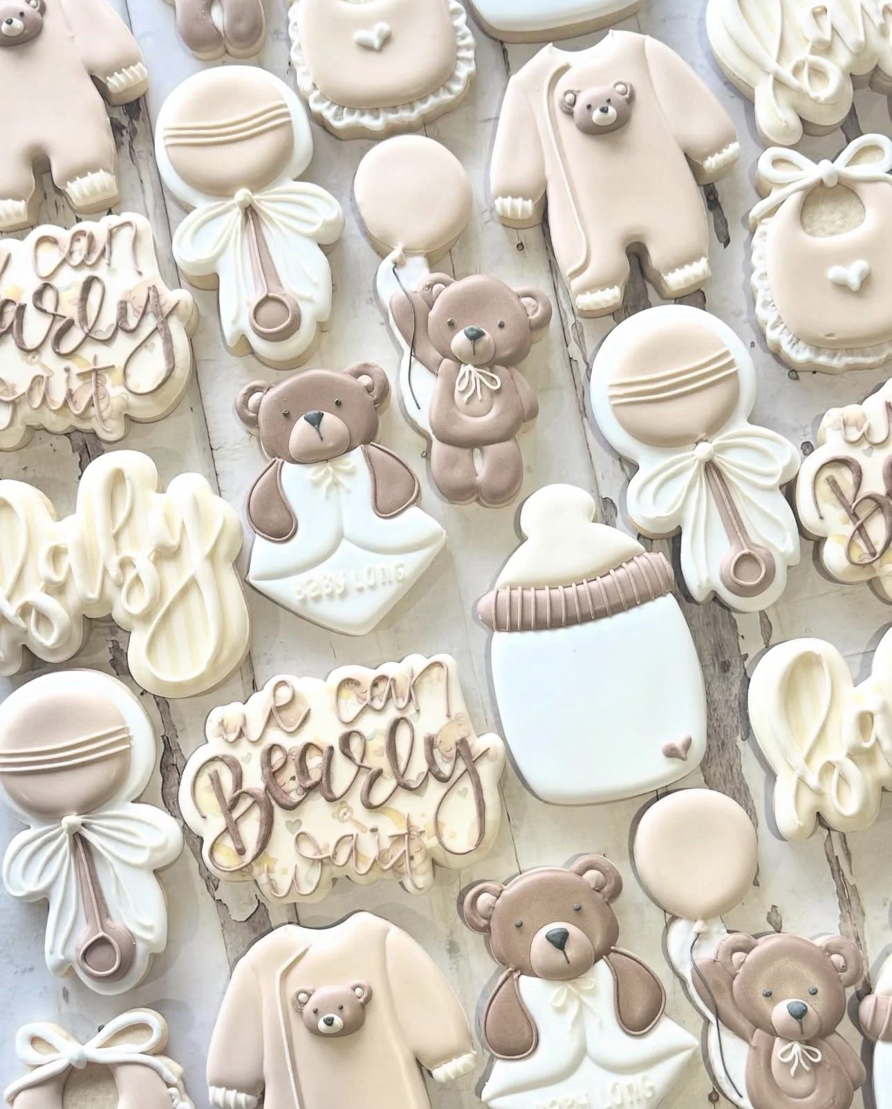 Pastel baby shower cookies decorated with teddy bears, baby onesies, rattles, bottles, bows, and congratulatory messages