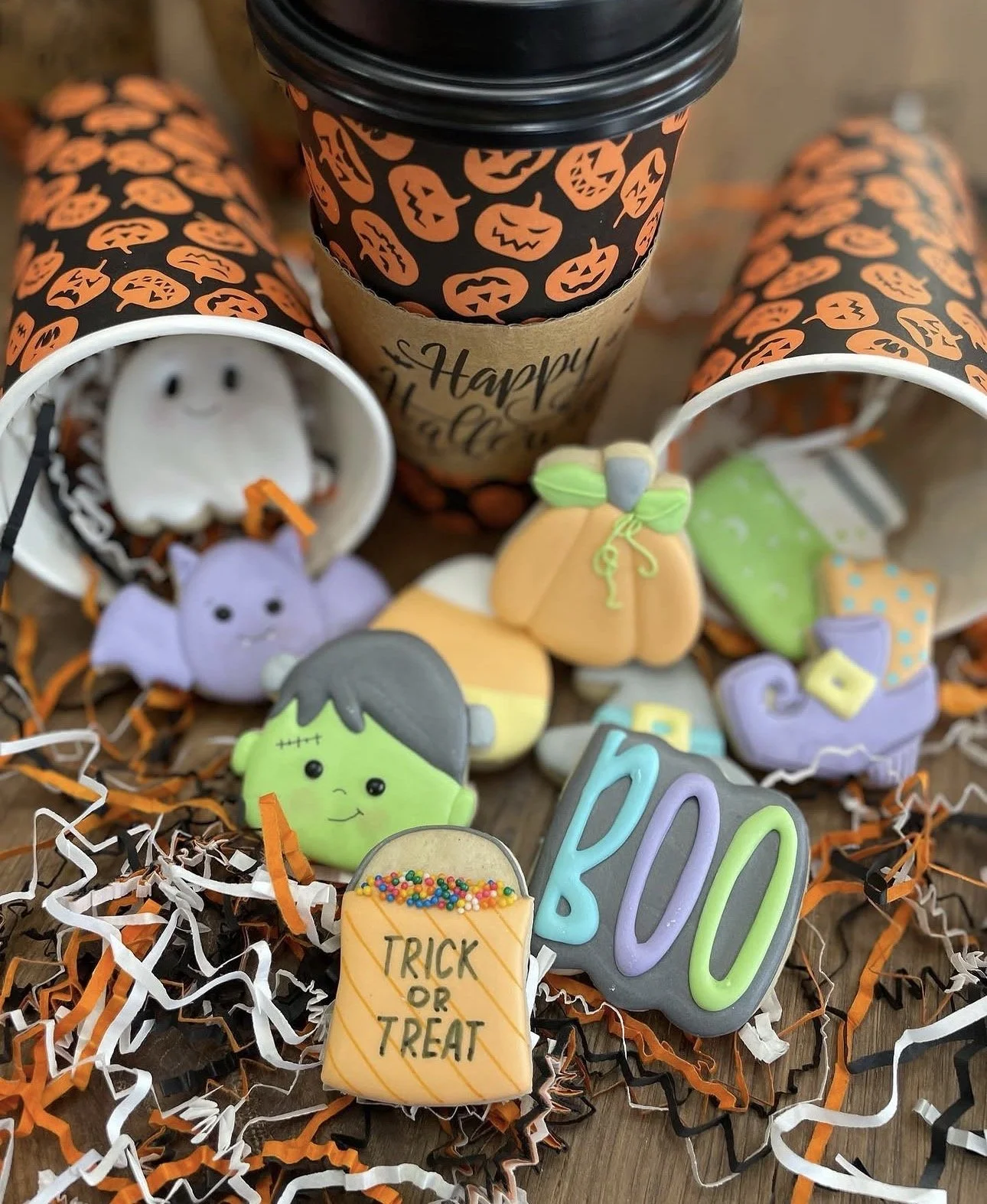 Halloween-themed coffee cup and decorated cookies featuring pumpkins, ghosts, bats, Frankenstein, and a “Trick or Treat” message