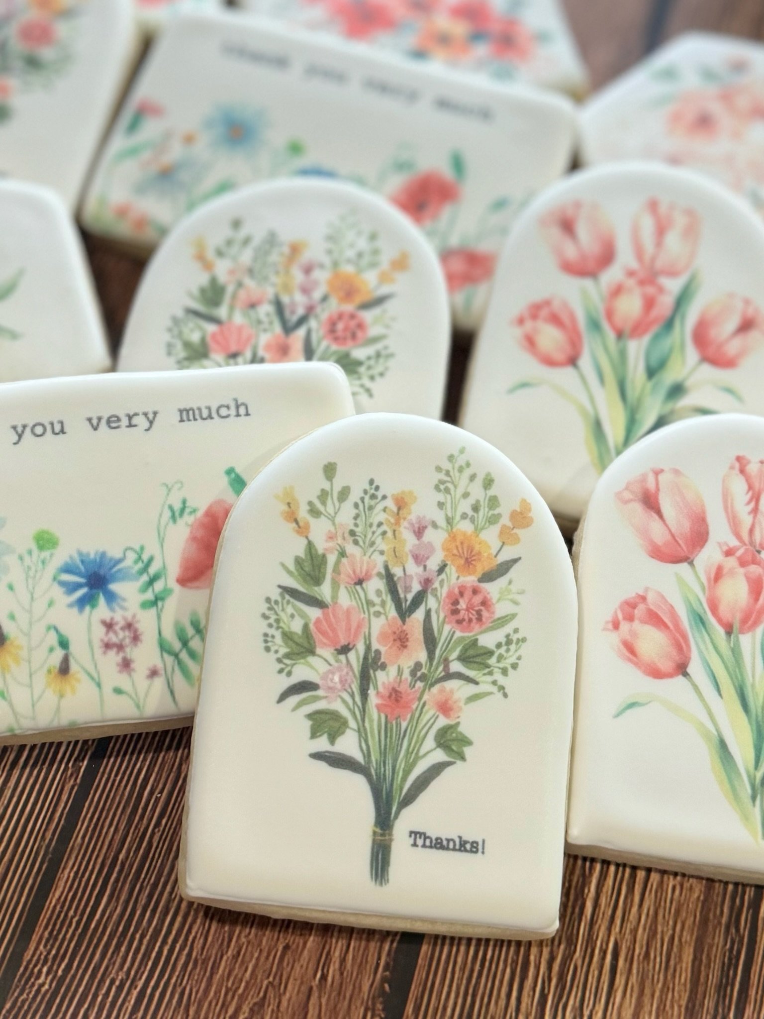 Assorted floral greeting cards featuring watercolor bouquets, tulips, wildflowers, and messages on a wooden table