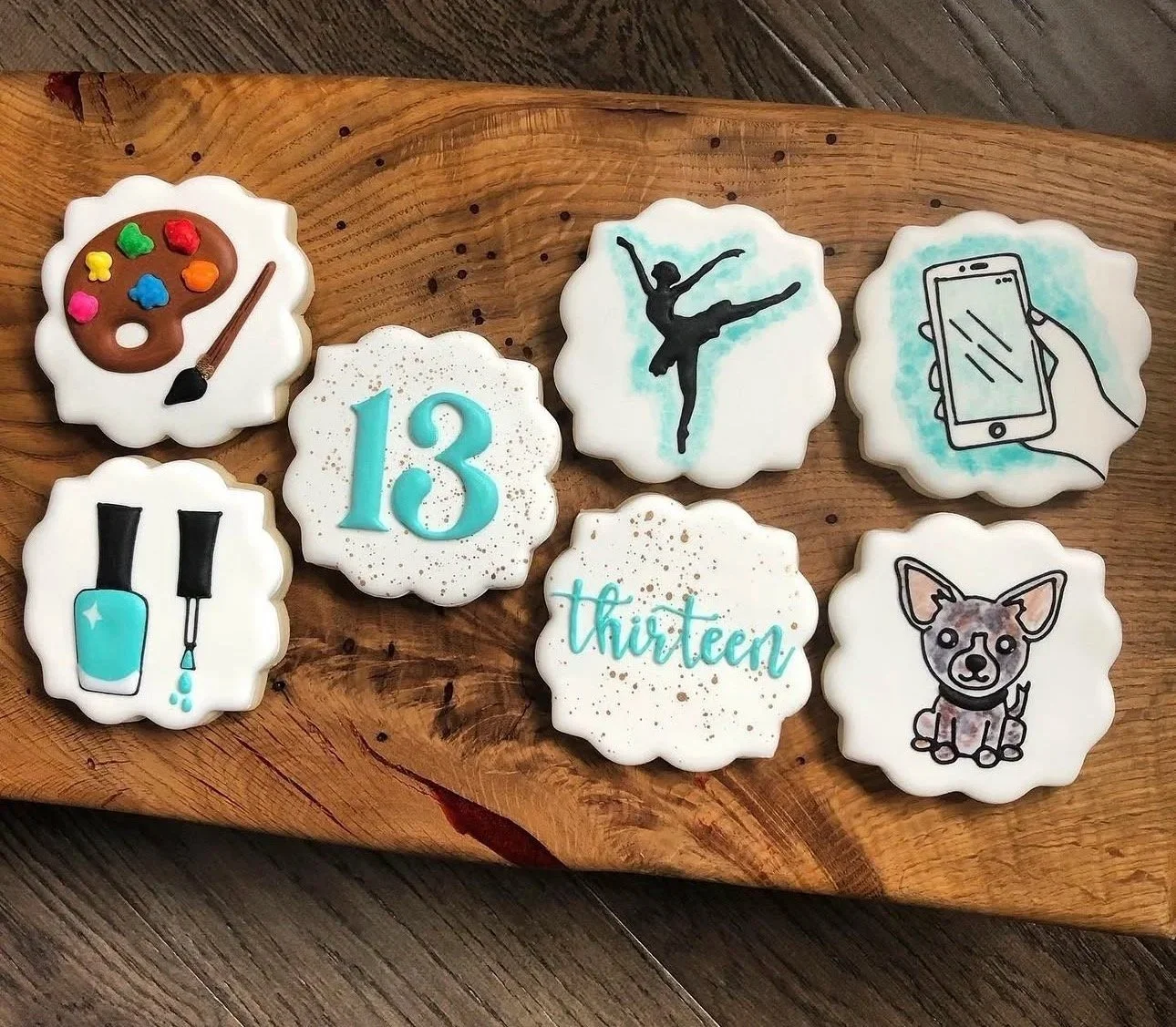 Decorated birthday cookies spelling “13” and “Thirteen,” with designs of a paint palette, nail polish, ballerina, smartphone, and Chihuahua.