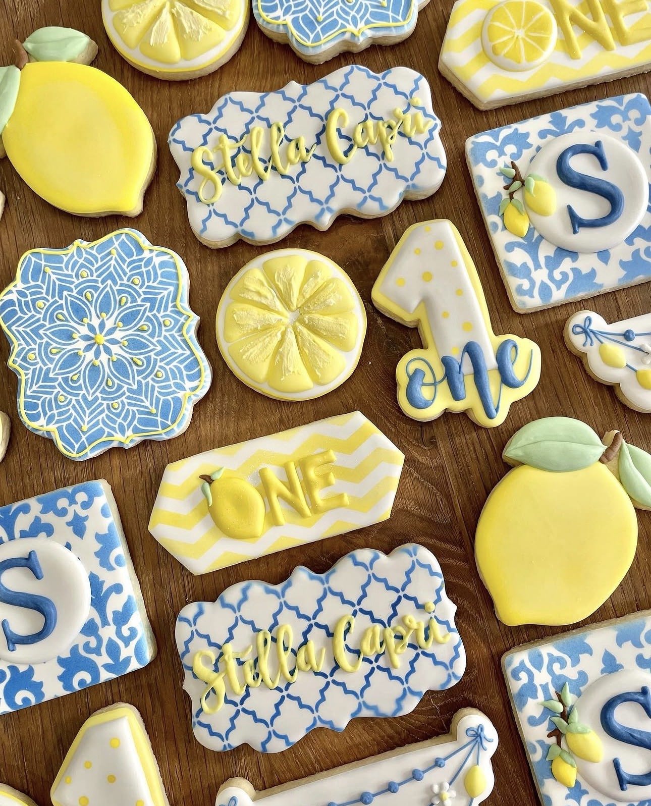 Decorated lemon-themed sugar cookies on a wooden table, featuring blue-and-white patterns, lemons, and yellow cursive lettering reading “Squeeze the Day.”