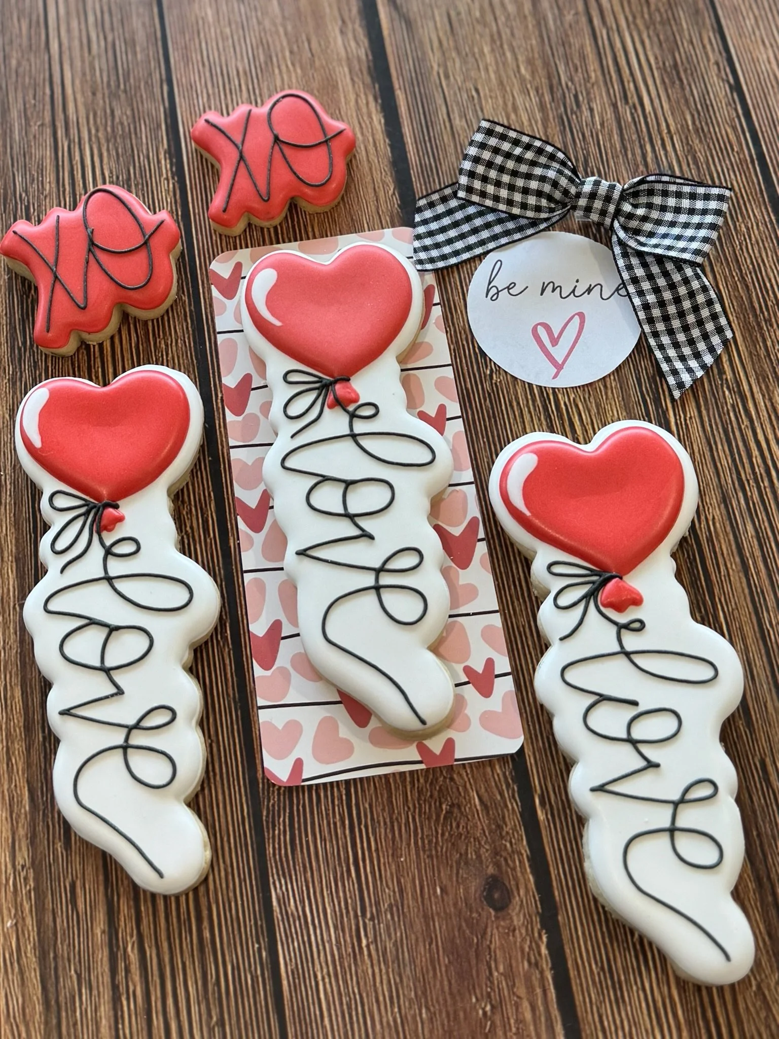Valentine's Day heart-shaped cookies with red and white icing, black drizzle, and a gingham bow on a wood table