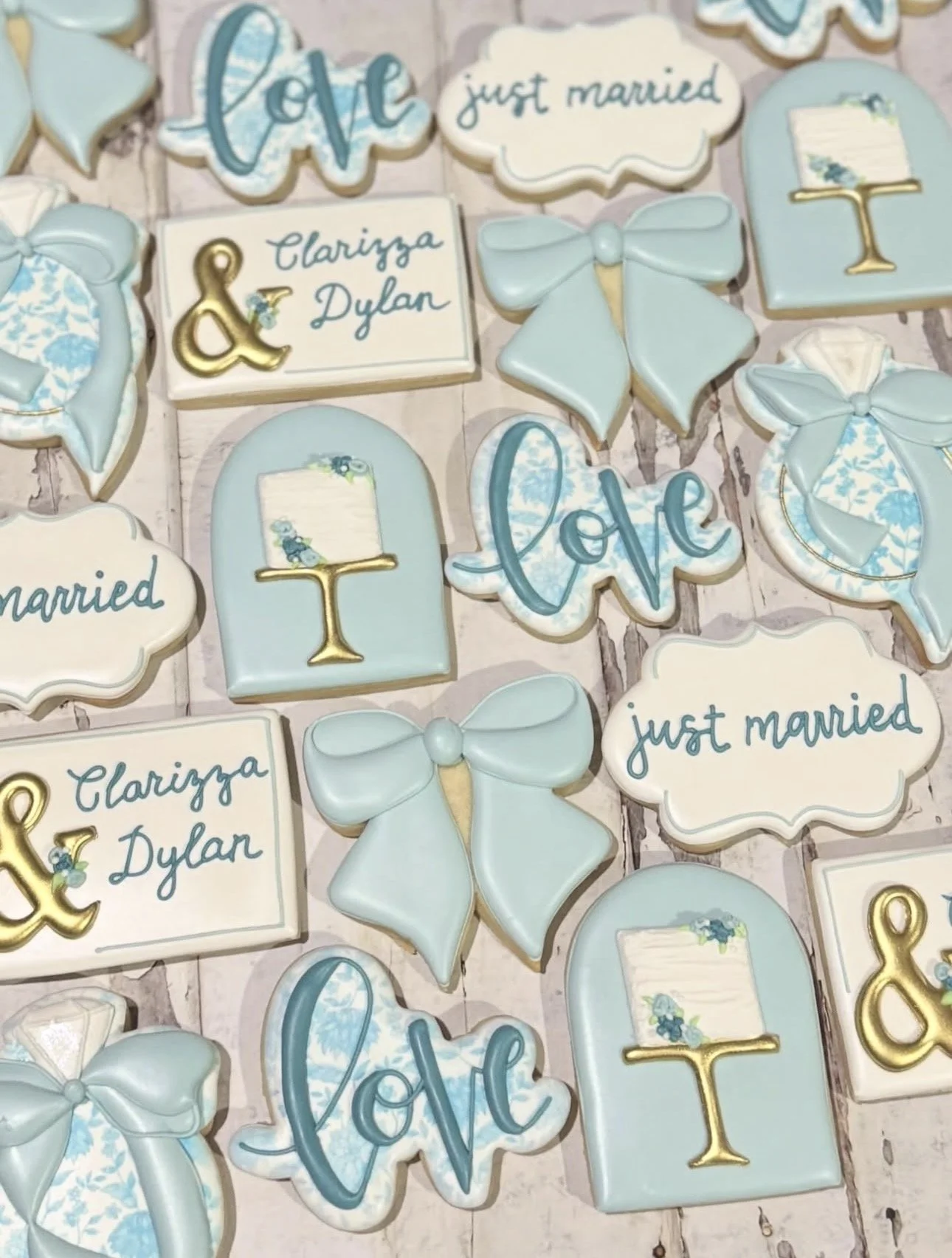Decorated wedding cookies in blue and white with bows, rings, floral accents, and messages reading “just married” and “Clariyza & Dylan.”