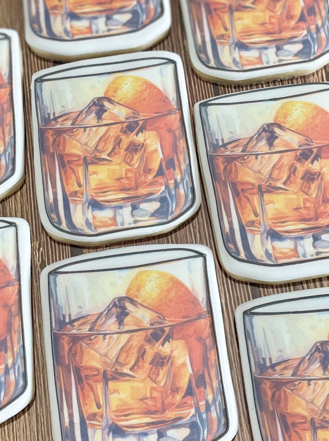 Repeated watercolor-style illustrations of whiskey glasses with ice and orange slices on a wood-grain background