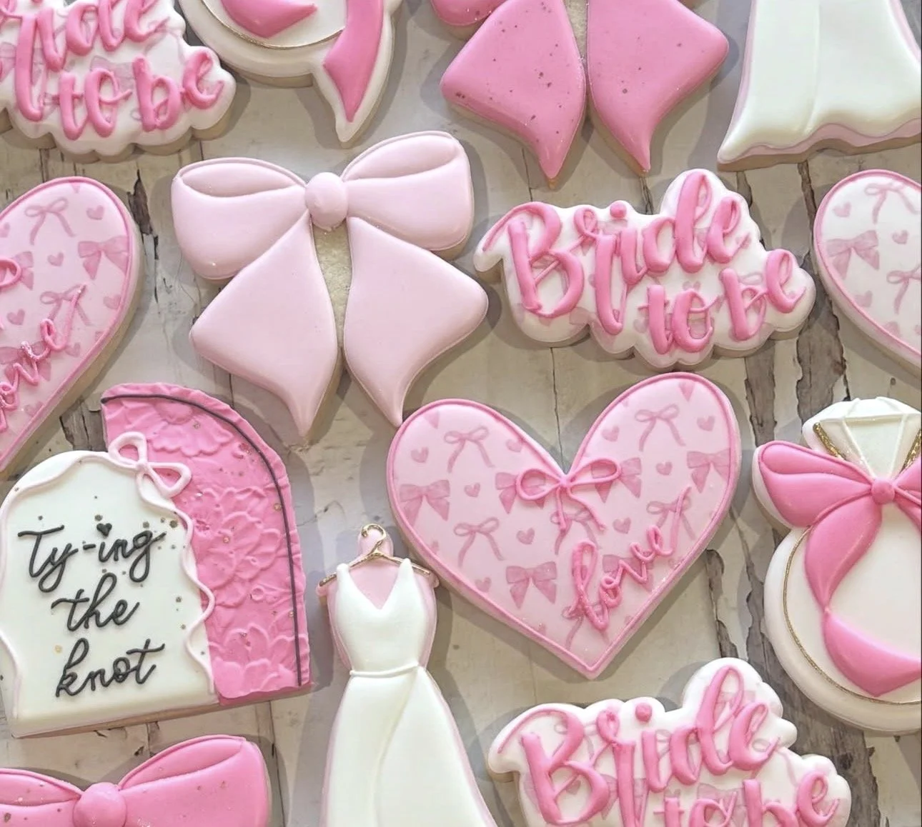 Pink and white bridal shower cookies decorated with bows, hearts, wedding dresses, and "Bride to Be" lettering