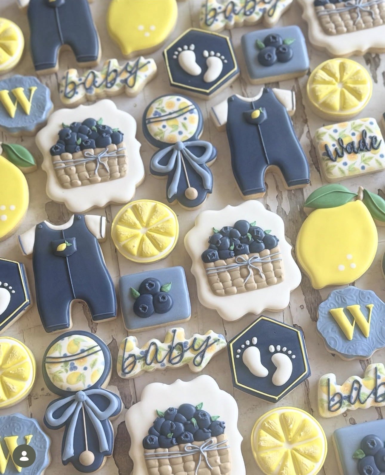 Assorted decorated cookies featuring lemons, blueberries, baby onesies, bows, baby footprints, and the words “baby” and “welcome.”
