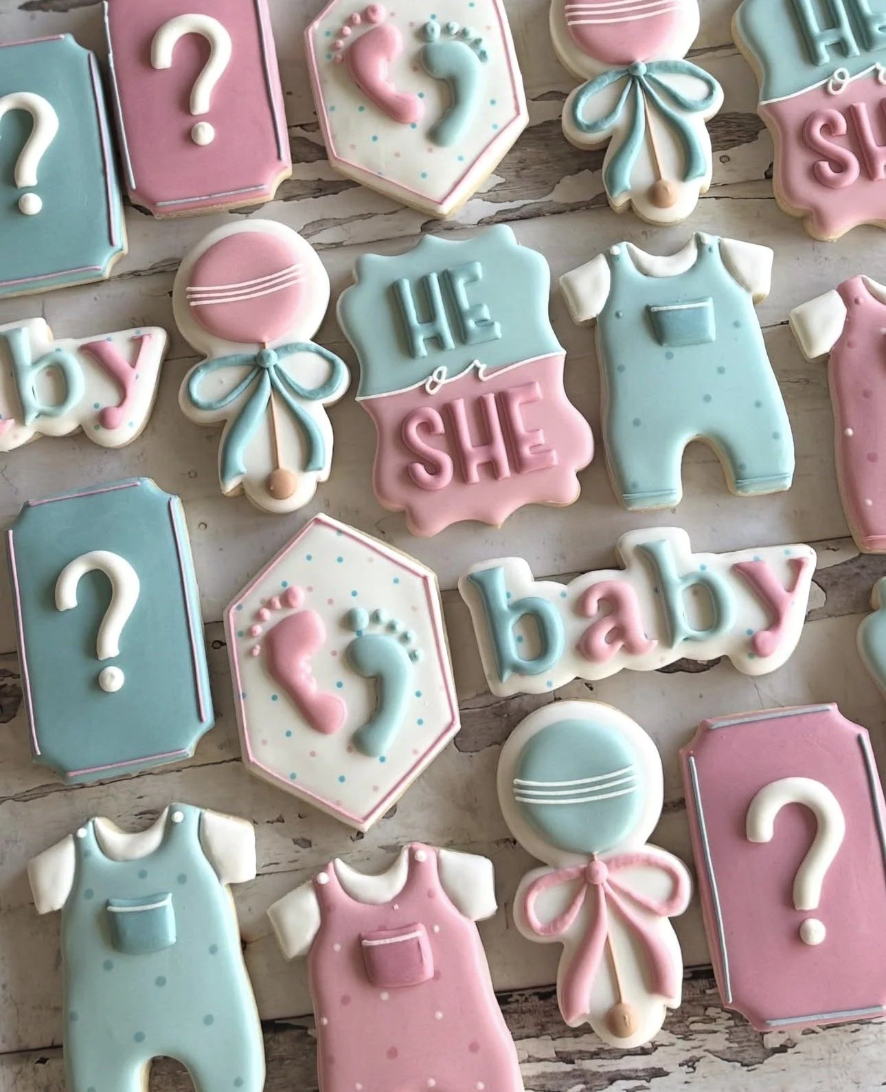 Pastel pink and blue baby shower sugar cookies featuring question marks, baby footprints, onesies, balloons, and “He or She” and “baby” lettering.
