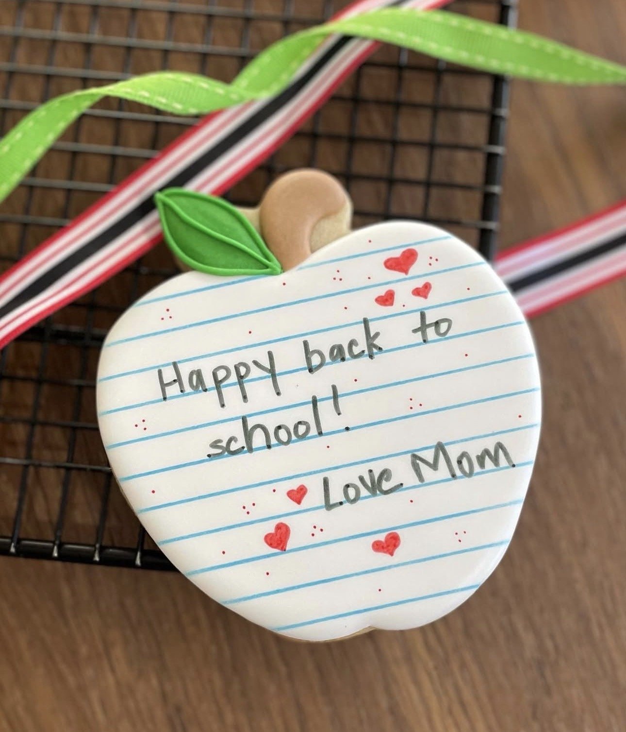 Apple-shaped back-to-school sign reading “Happy back to school! Love Mom,” decorated with red hearts and a green leaf.