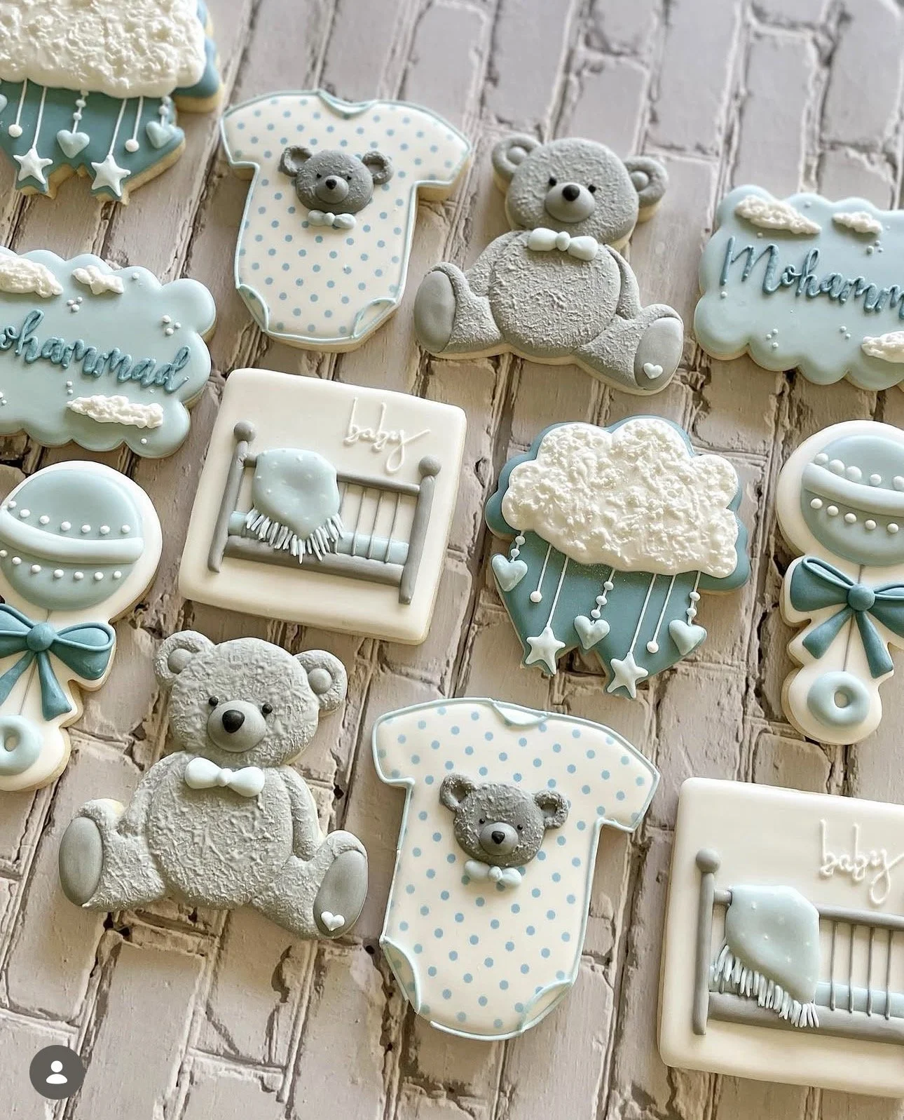 Baby shower cookies decorated with teddy bears, baby onesies, cribs, balloons, bows, clouds, and blue-and-white accents on a wood background