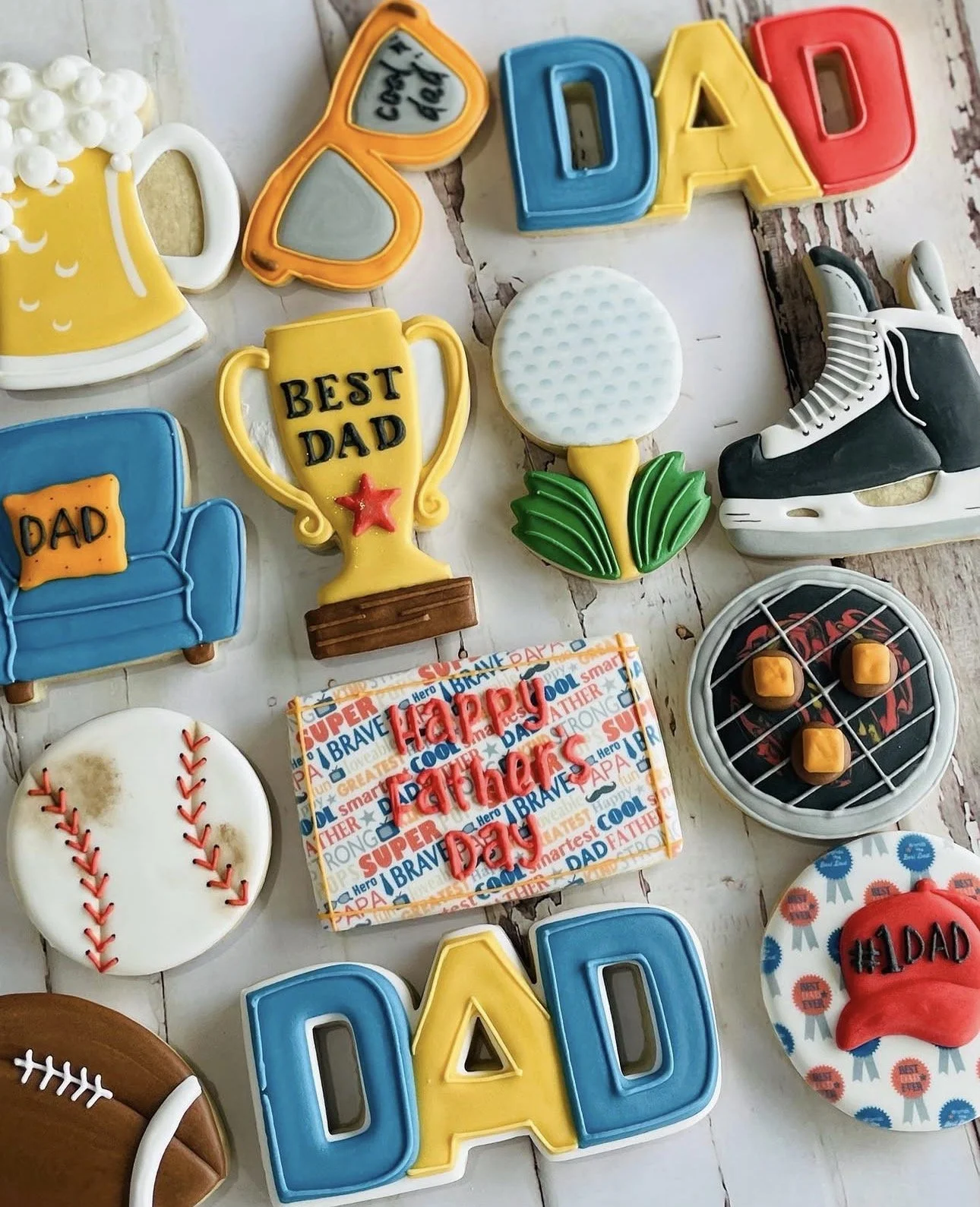 Colorful Father's Day cookies decorated with “DAD,” “Best Dad,” sports equipment, a trophy, golf club, hockey skate, baseball, football, and gift box.