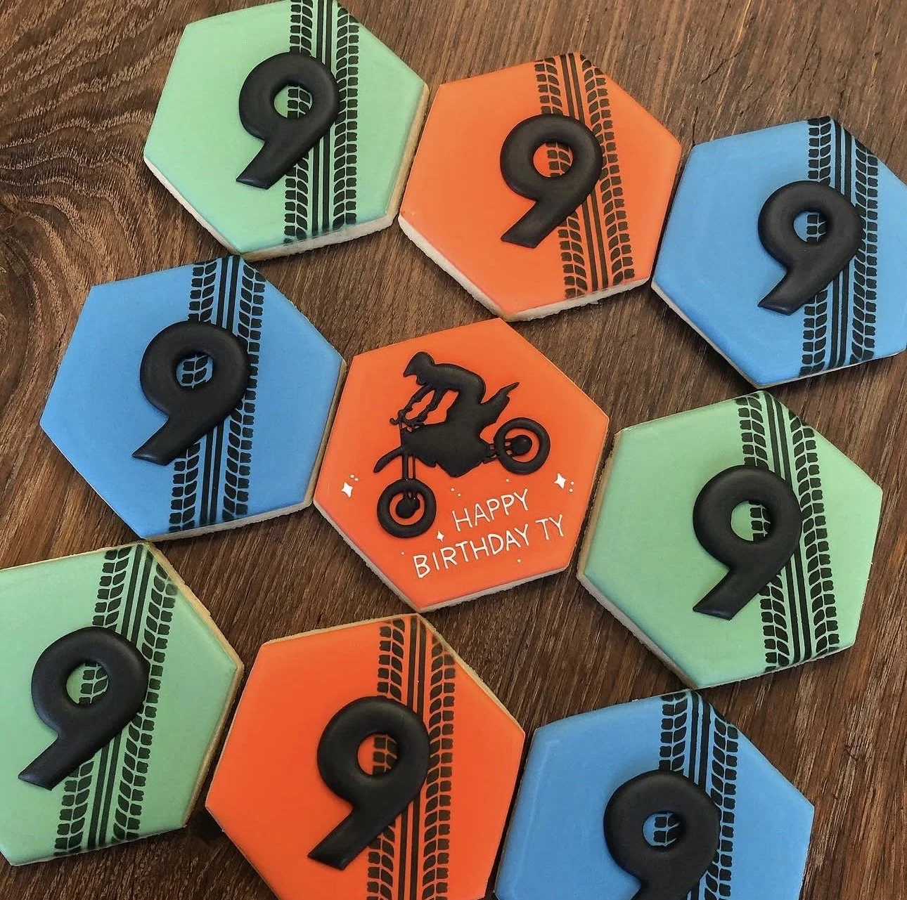 Colorful hexagonal motorcycle-themed birthday cookies with black tire-track designs and a central cookie reading “Happy Birthday Ty”.