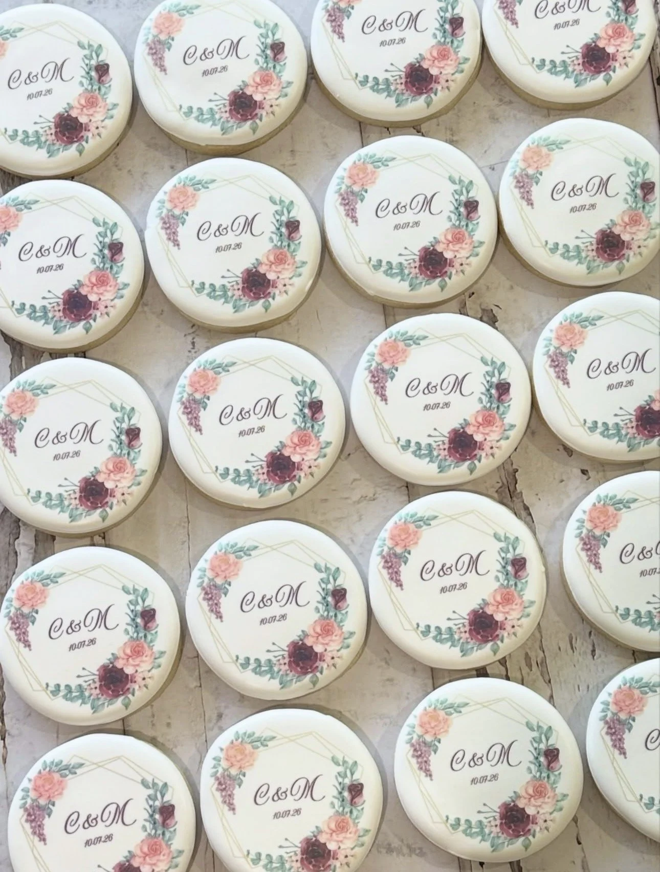 Rows of round floral wedding cookies decorated with the initials “C & M” and date “10.07.26.”