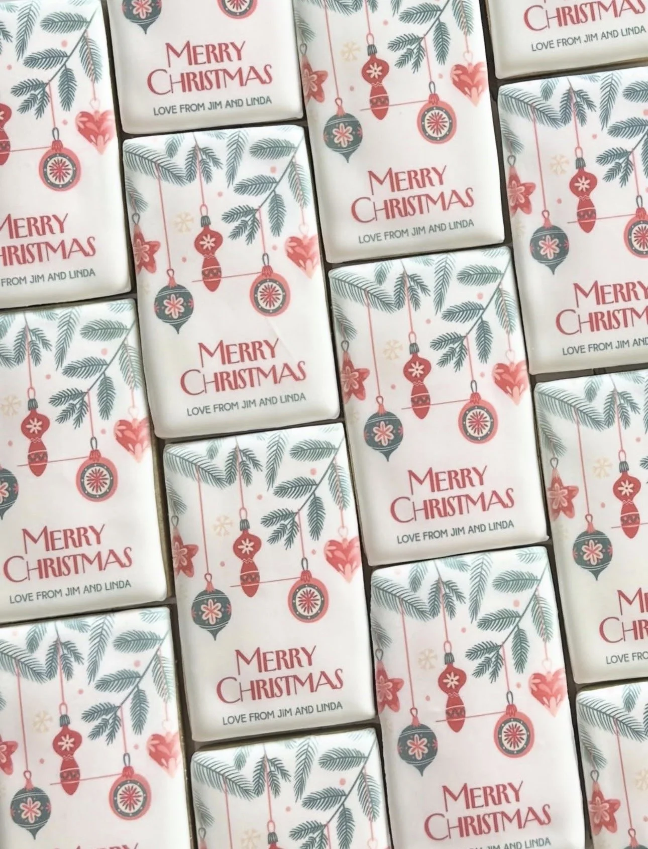 Pattern of personalized Christmas cards reading “Merry Christmas, Love from Jim and Linda,” decorated with vintage ornaments and evergreen branches.