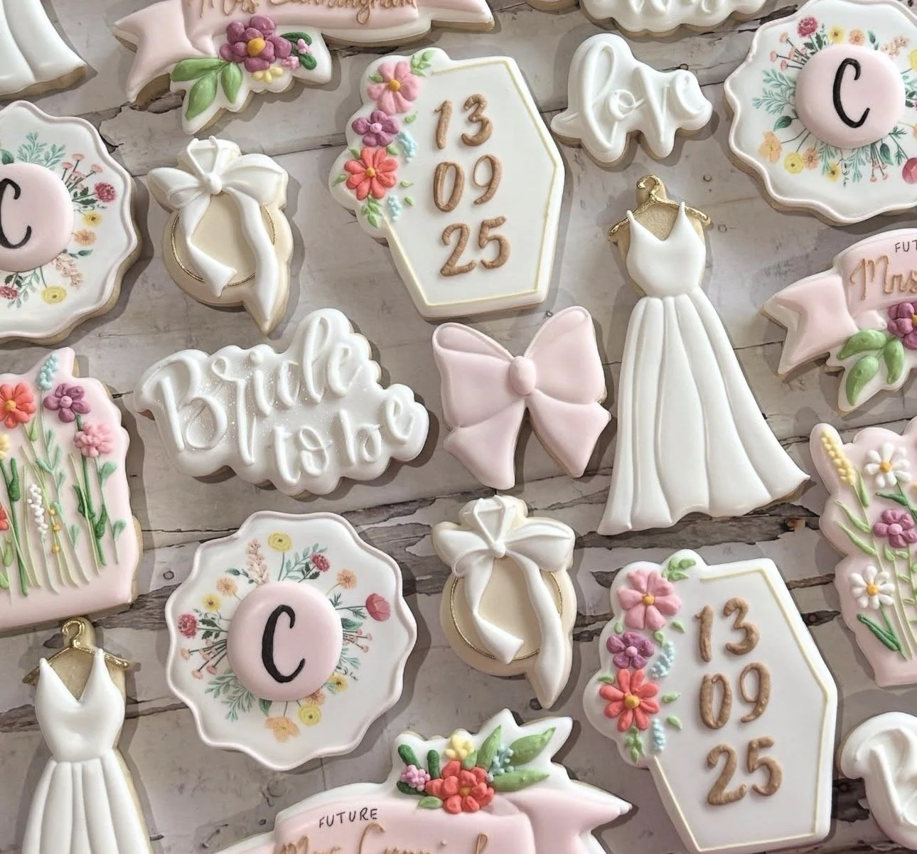 Decorated cookies featuring floral monogram plaques, bridal gowns, bows, bells, and wedding date cookies on a rustic surface