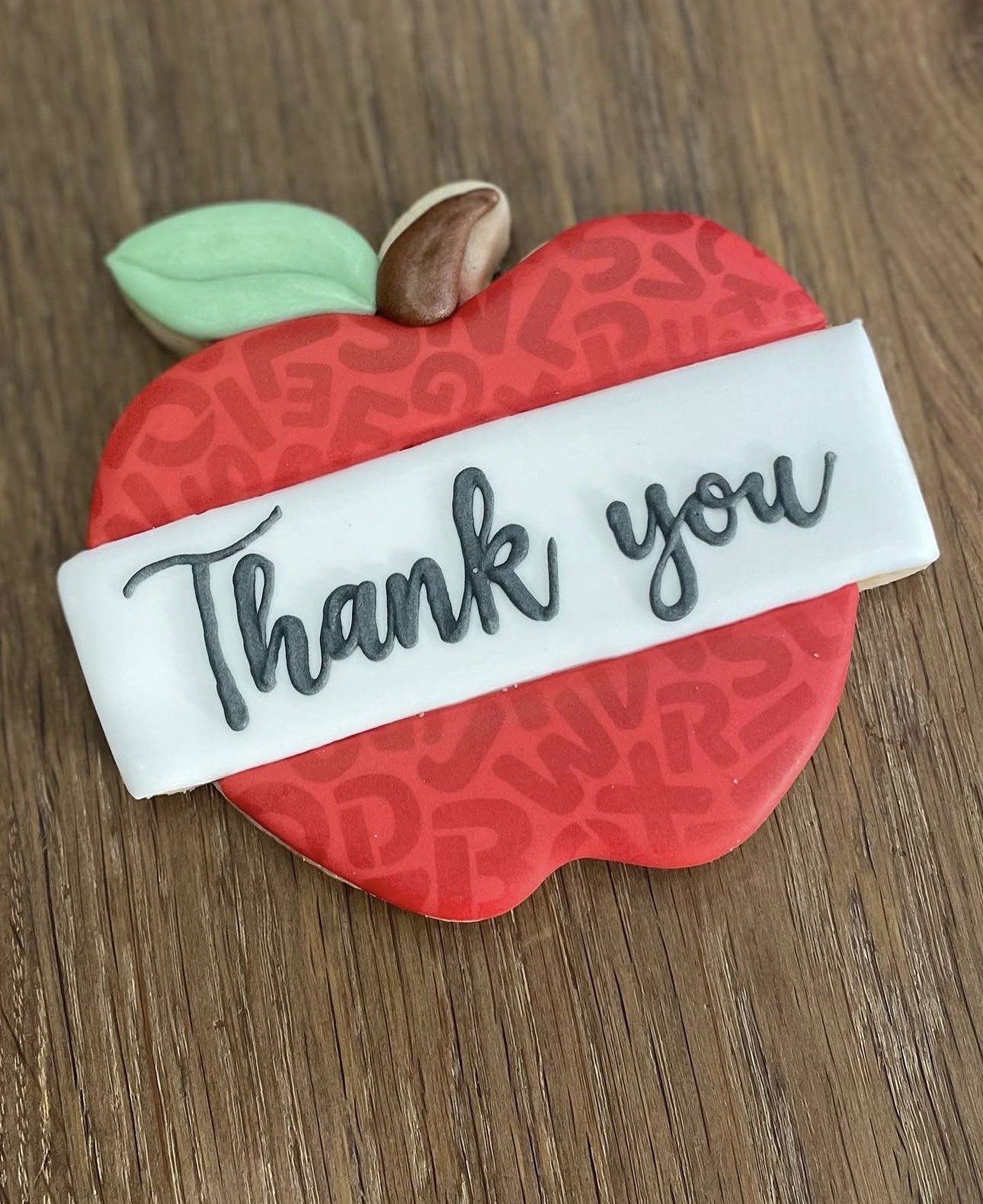 Decorated red apple-shaped cookie with green leaves, a brown stem, and a white banner reading “Thank You.”