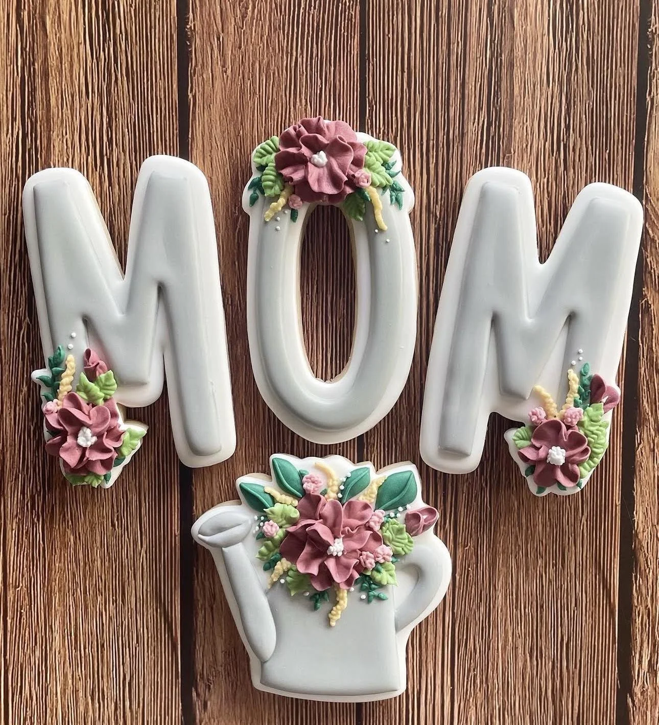 White ceramic MOM wall decor with colorful floral embellishments and a flower-filled hand-shaped vase on a wood background
