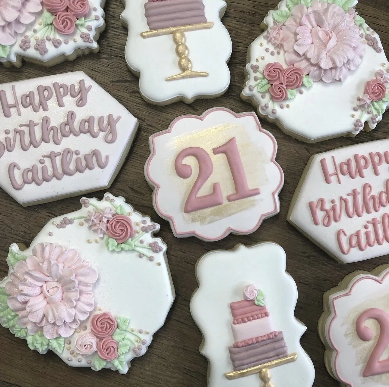 Decorated pink and white birthday cookies featuring floral designs, tiered cakes, and “Happy Birthday Caitlin” and “21” lettering
