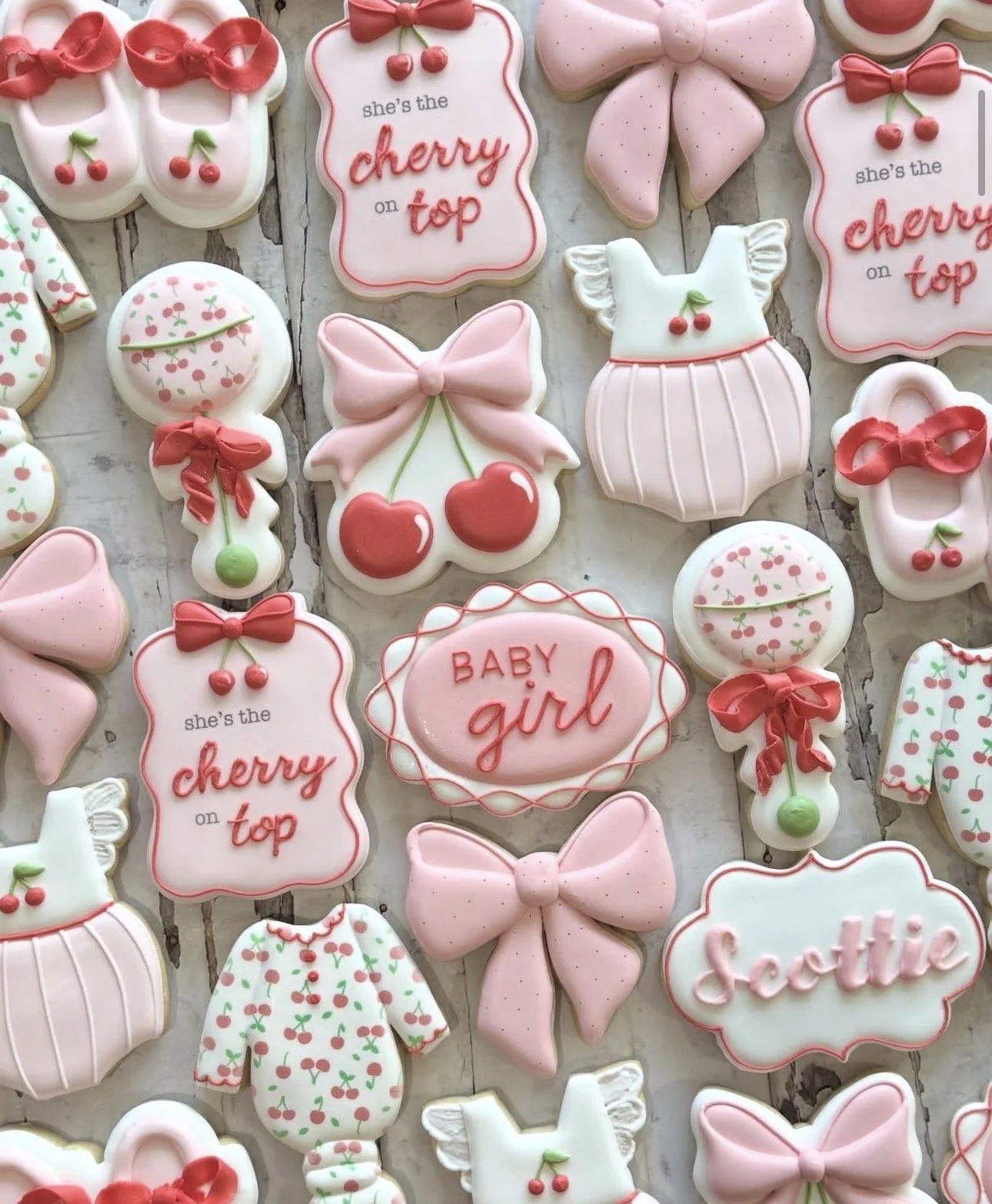Decorated baby shower sugar cookies with pink bows, cherries, baby outfits, and messages including “Baby girl” and “She’s the cherry on top.”