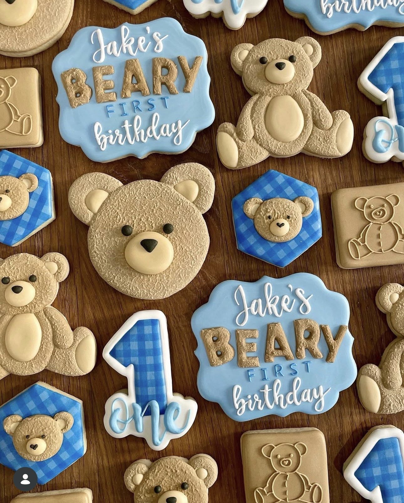 Blue and tan teddy bear-themed first birthday cookies, including “Jake’s Baby First Birthday” message cookies, bear shapes, blue gingham accents, and a number one cookie.