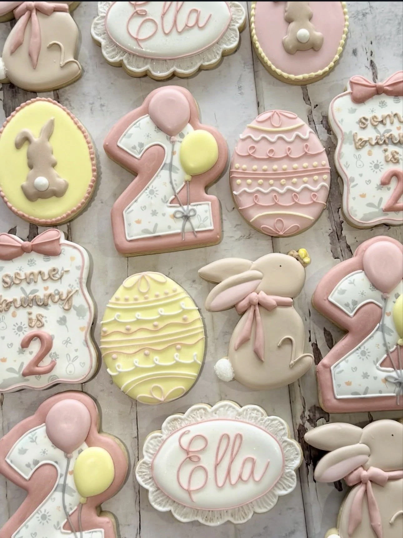 Pastel pink and yellow Easter baby shower cookies decorated with bunnies, eggs, balloons, bows, and “Baby” lettering