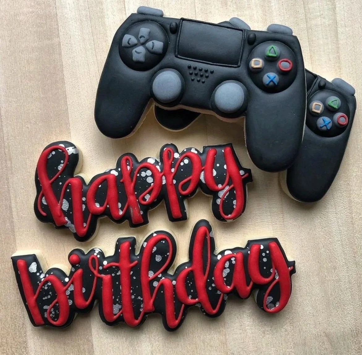 Black PlayStation game controller-themed cake with red-and-black “PlayStation” lettering on a wooden surface
