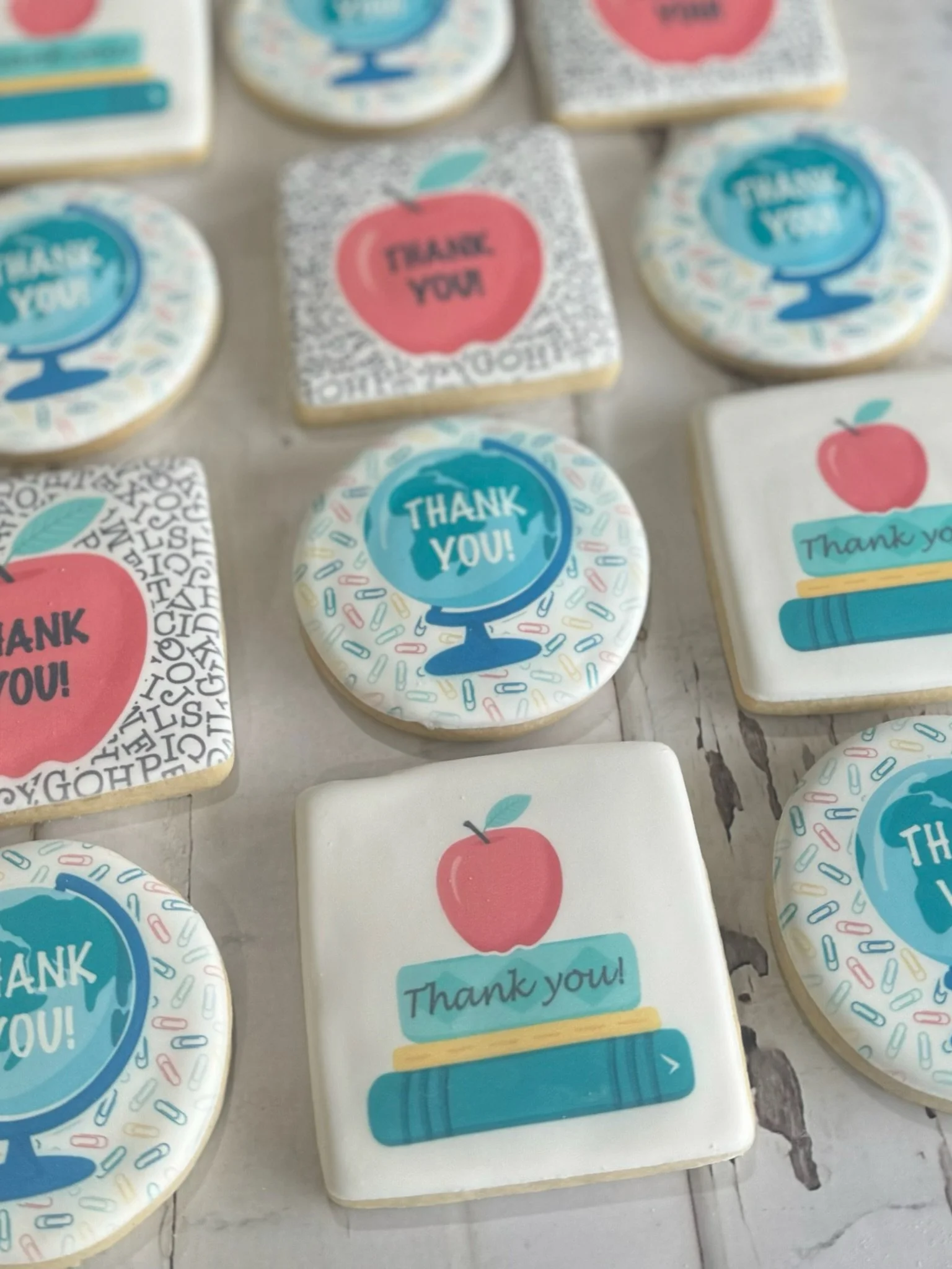 Assorted decorated thank-you sugar cookies featuring apples, globes, pencils, and colorful school-themed designs.