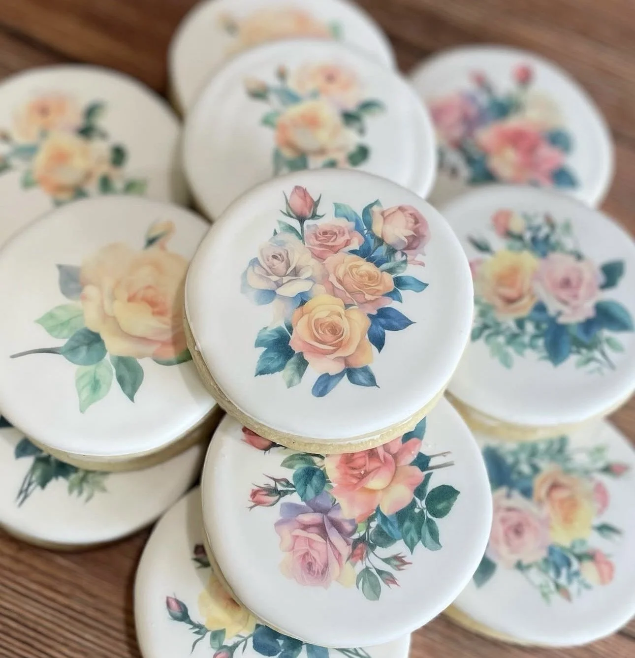 Stack of round white floral cookies decorated with pastel roses and green leaves on a wooden surface