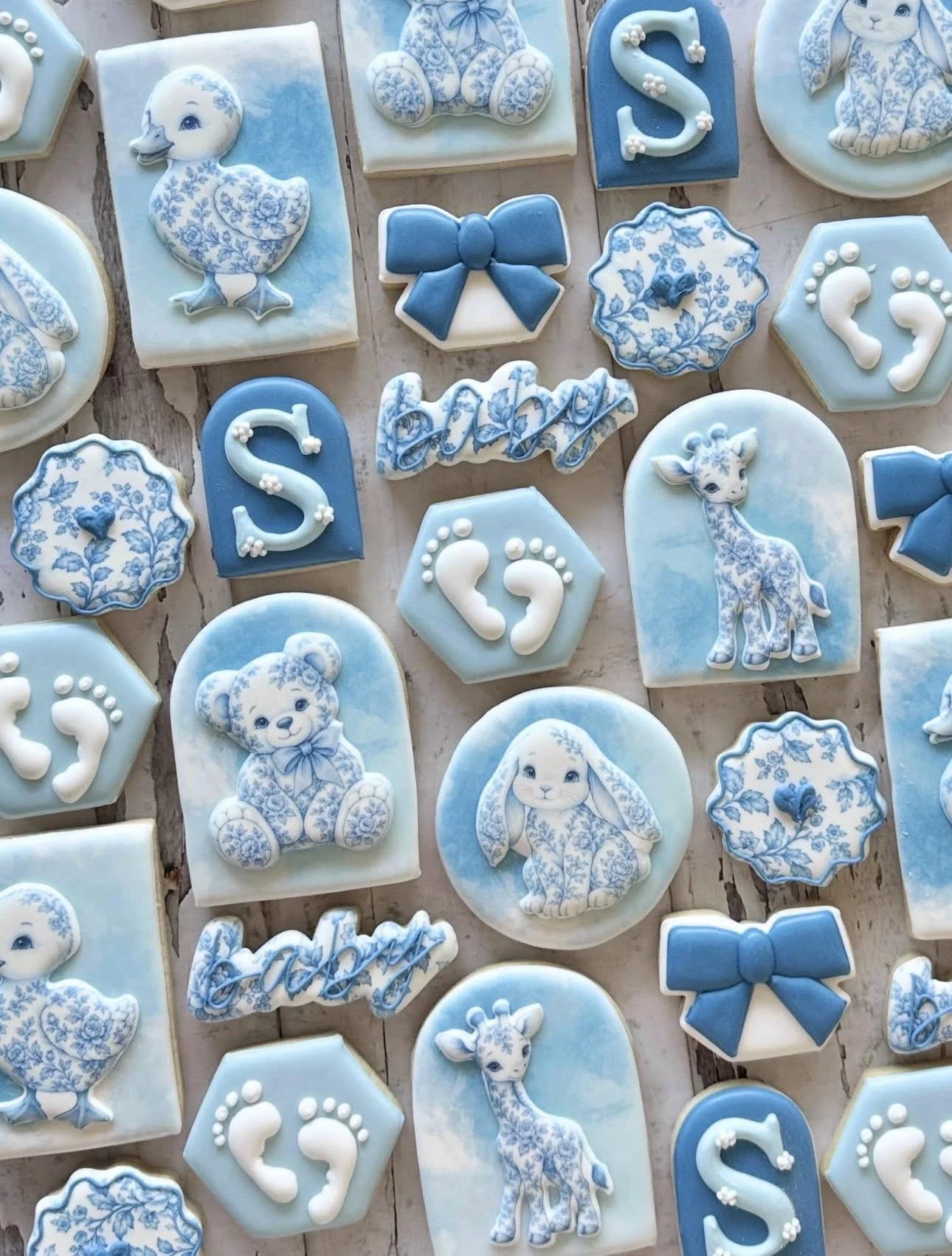 Blue and white baby shower cookies featuring floral animals, bows, baby footprints, and letter S designs