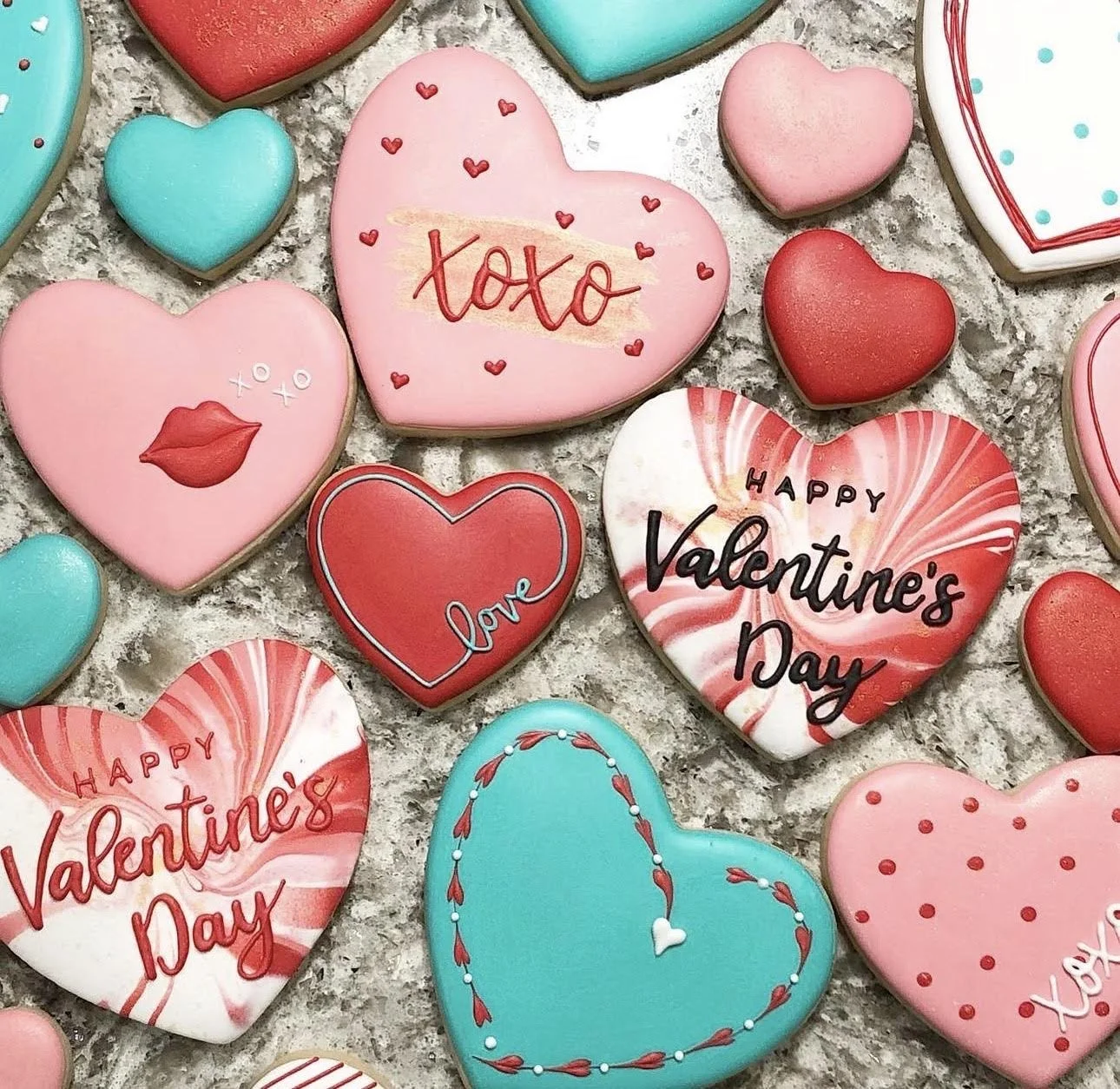 Assorted heart-shaped Valentine's Day cookies decorated in pink, red, turquoise, and white, with messages including “XOXO,” “Love,” and “Happy Valentine’s Day.”
