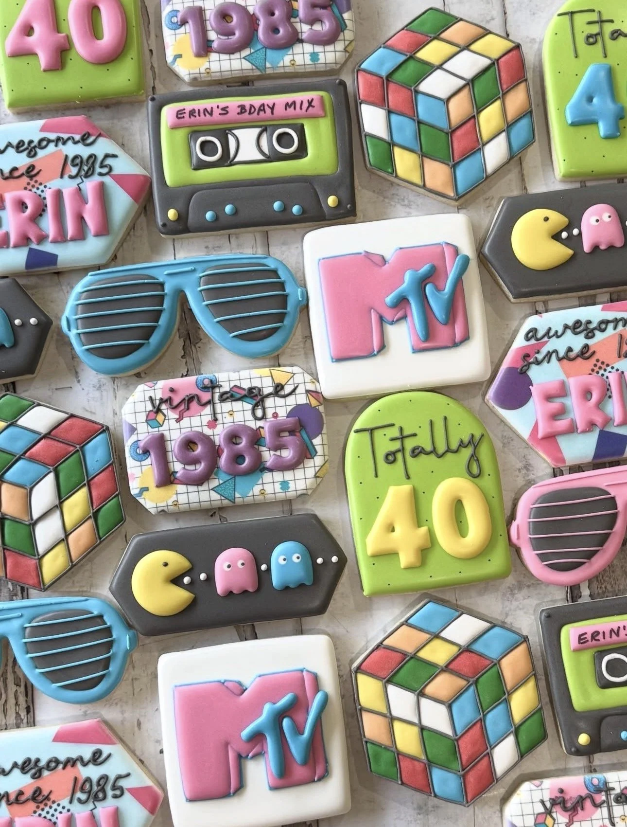 Colorful retro-themed decorated cookies featuring Rubik’s cubes, cassette tapes, Pac-Man, sunglasses, MTV logos, and 40th birthday designs.